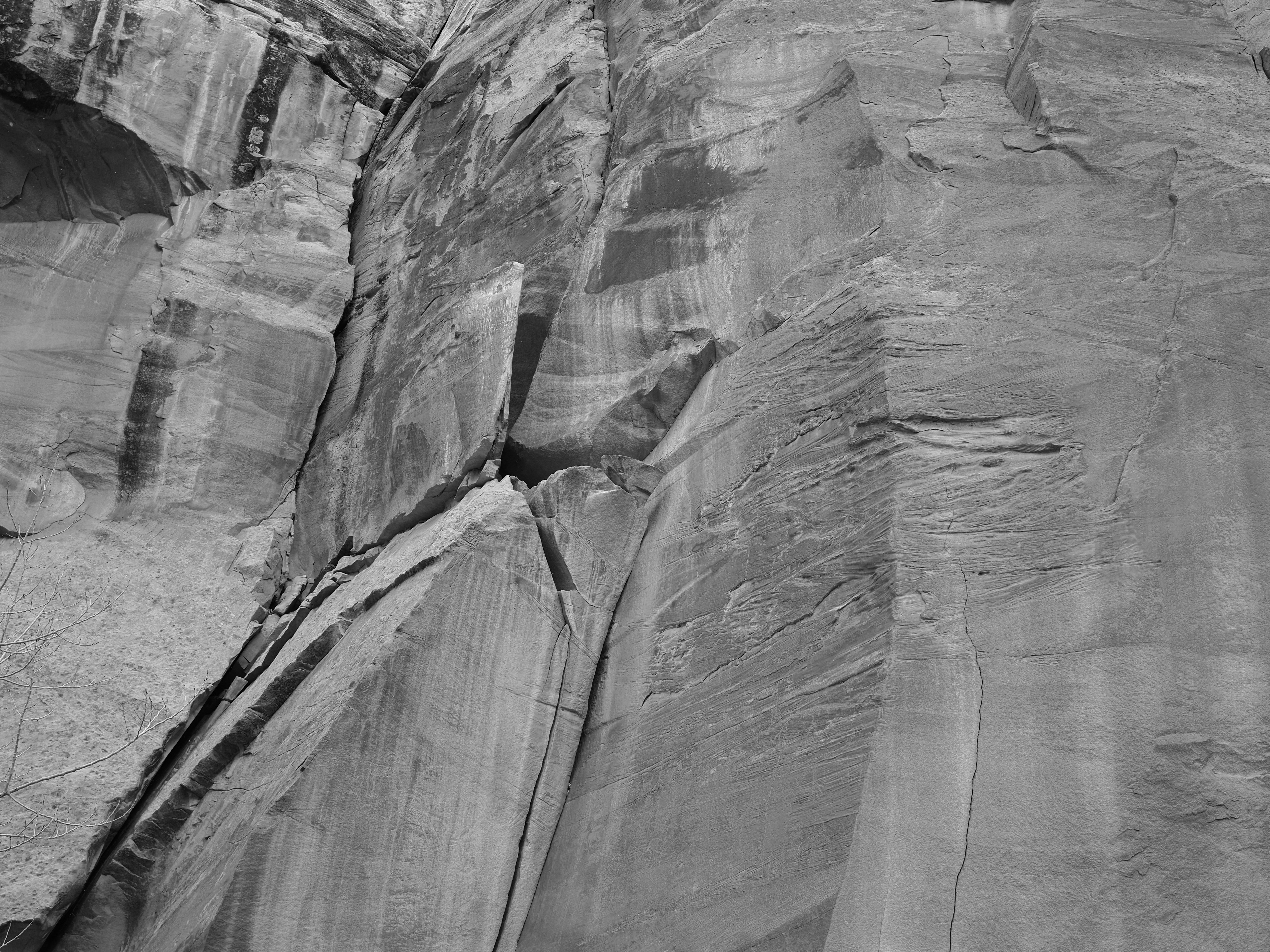 A towering grey sandstone cliff face with deep vertical fissures and layered rock textures