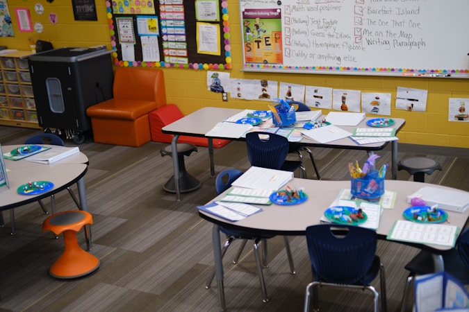 Empty elementary school classroom tables with student folders and supplies ready for the first day