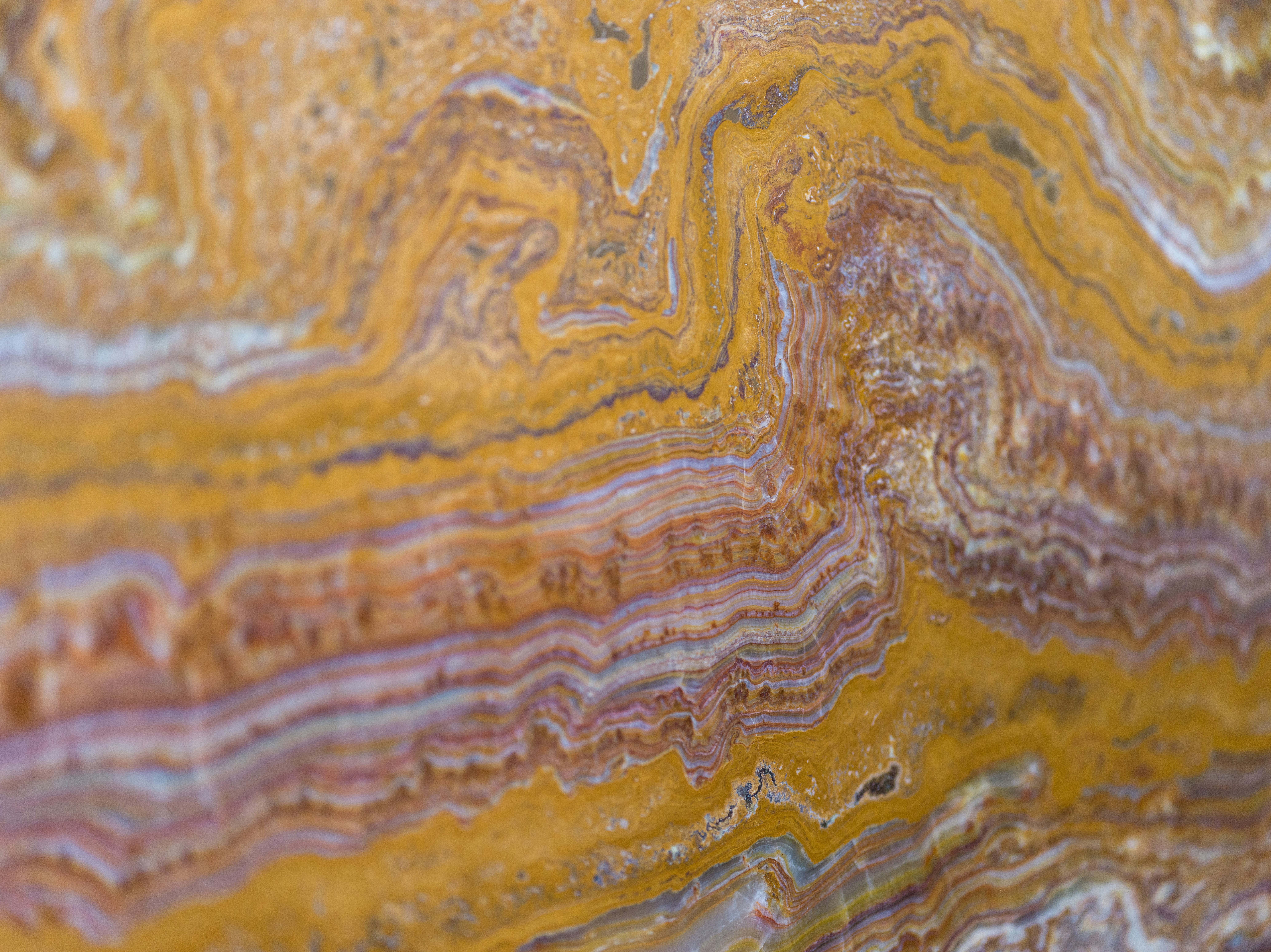 A polished slab of yellow and purple banded agate stone with swirling patterns