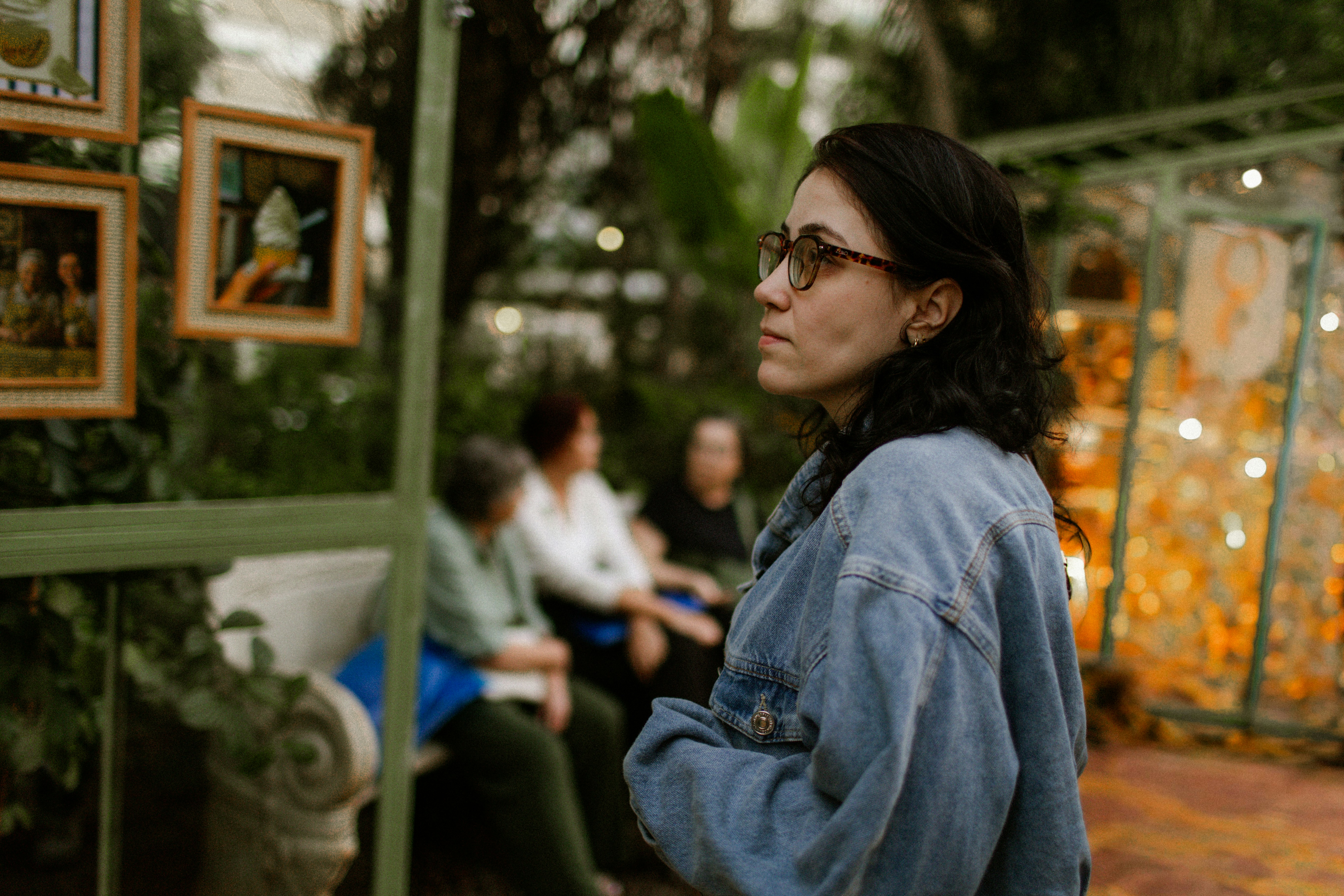 A woman in a denim jacket looking at framed art in a garden.