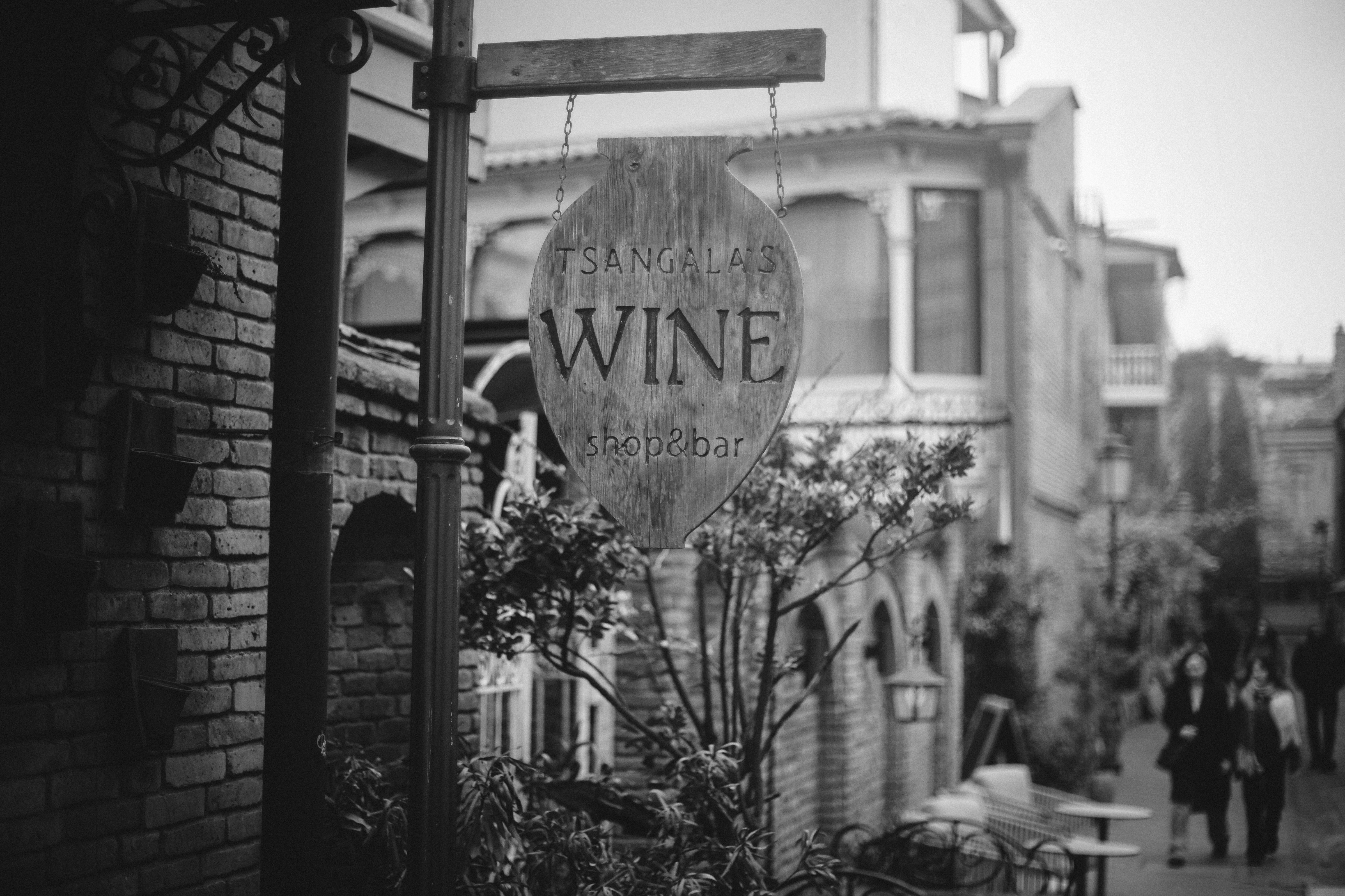 A wooden sign reading TSANGALA'S WINE shop&bar hanging on a city street