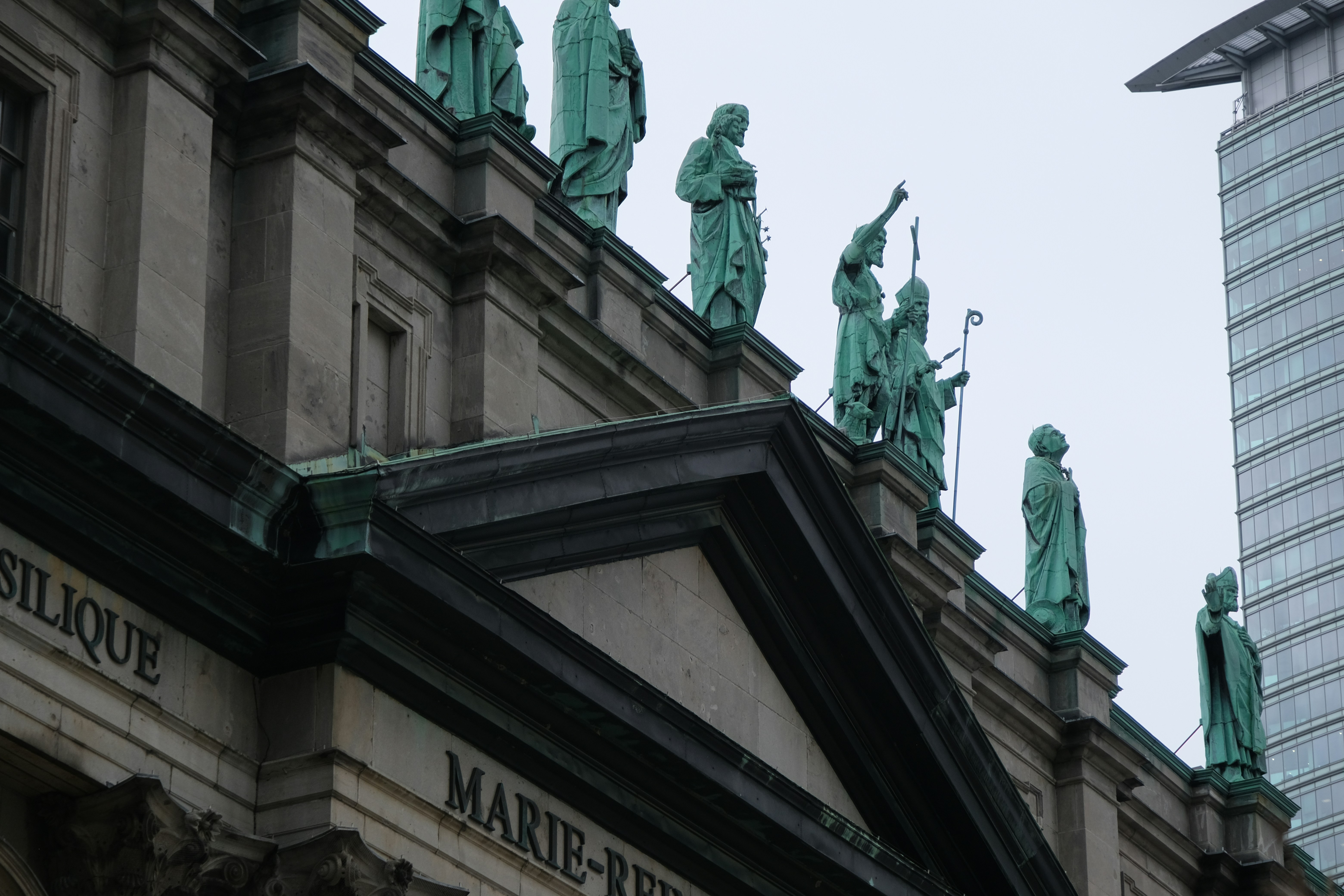 Green copper statues lining the roofline of a classical stone building in Montreal