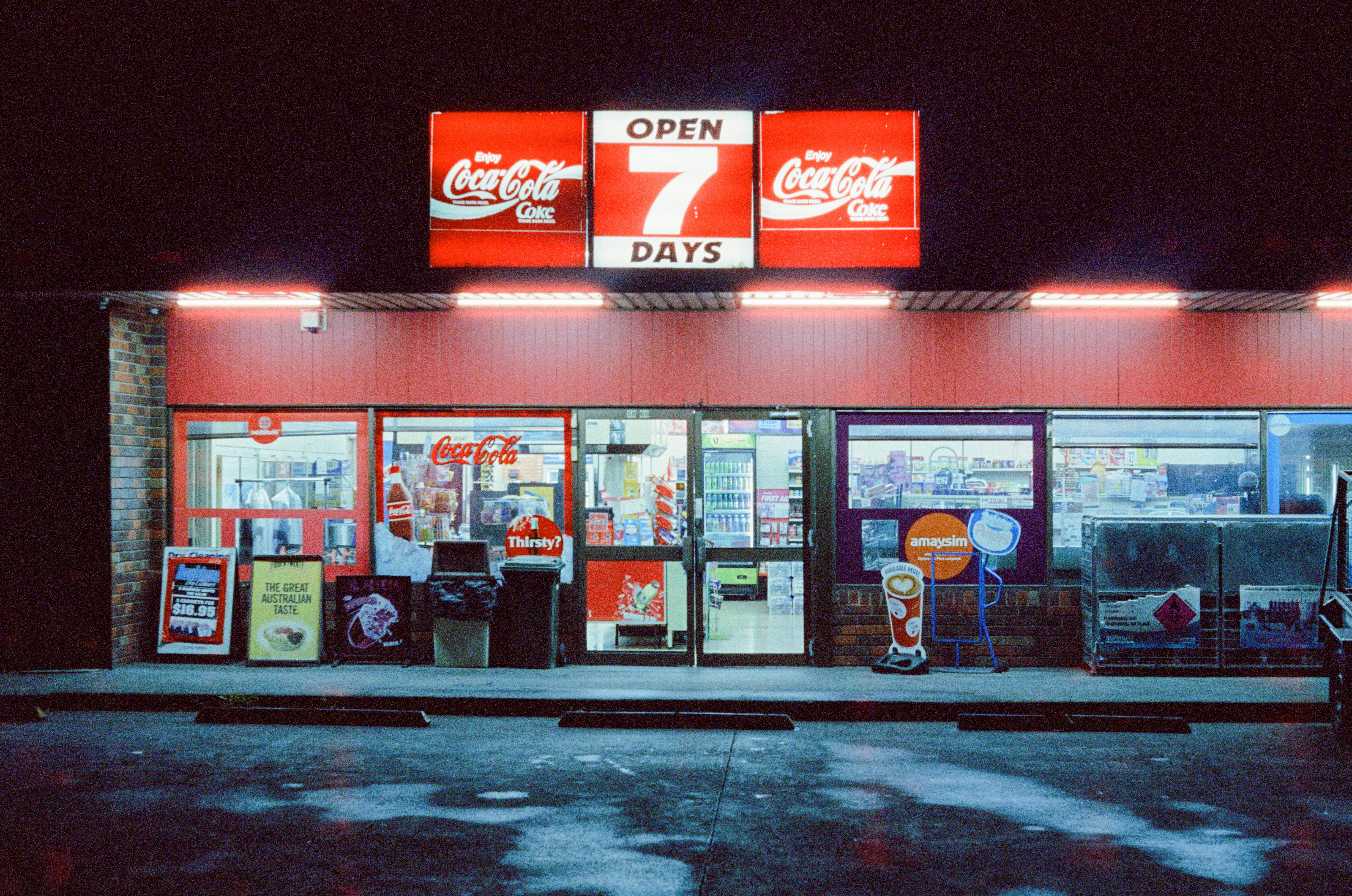 A convenience store at night with a sign reading "OPEN 7 DAYS" above the entrance.