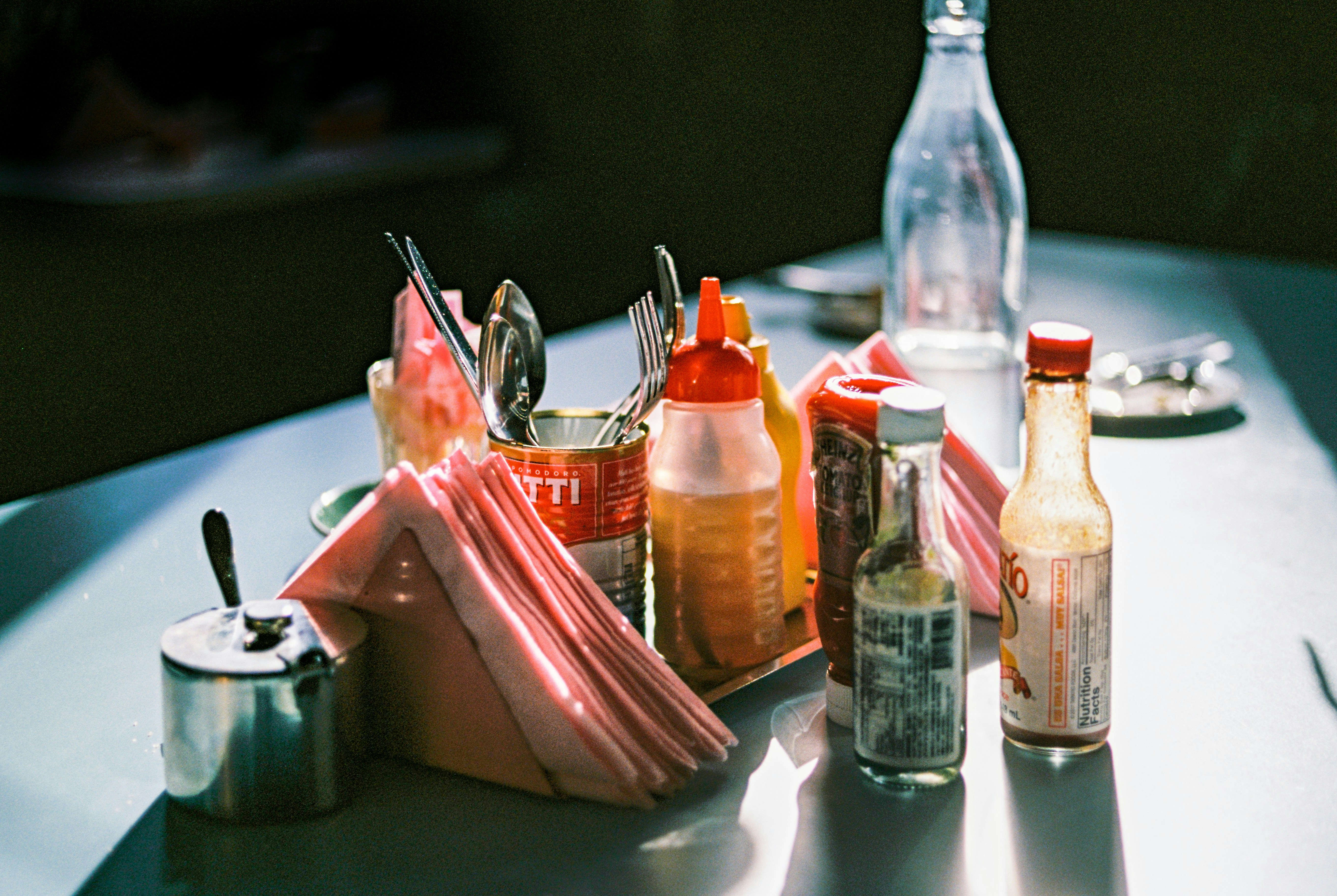 Condiments, napkins, and cutlery on a restaurant table in soft natural light.