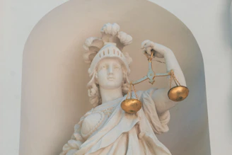A white marble statue of a woman in a helmet holding golden scales