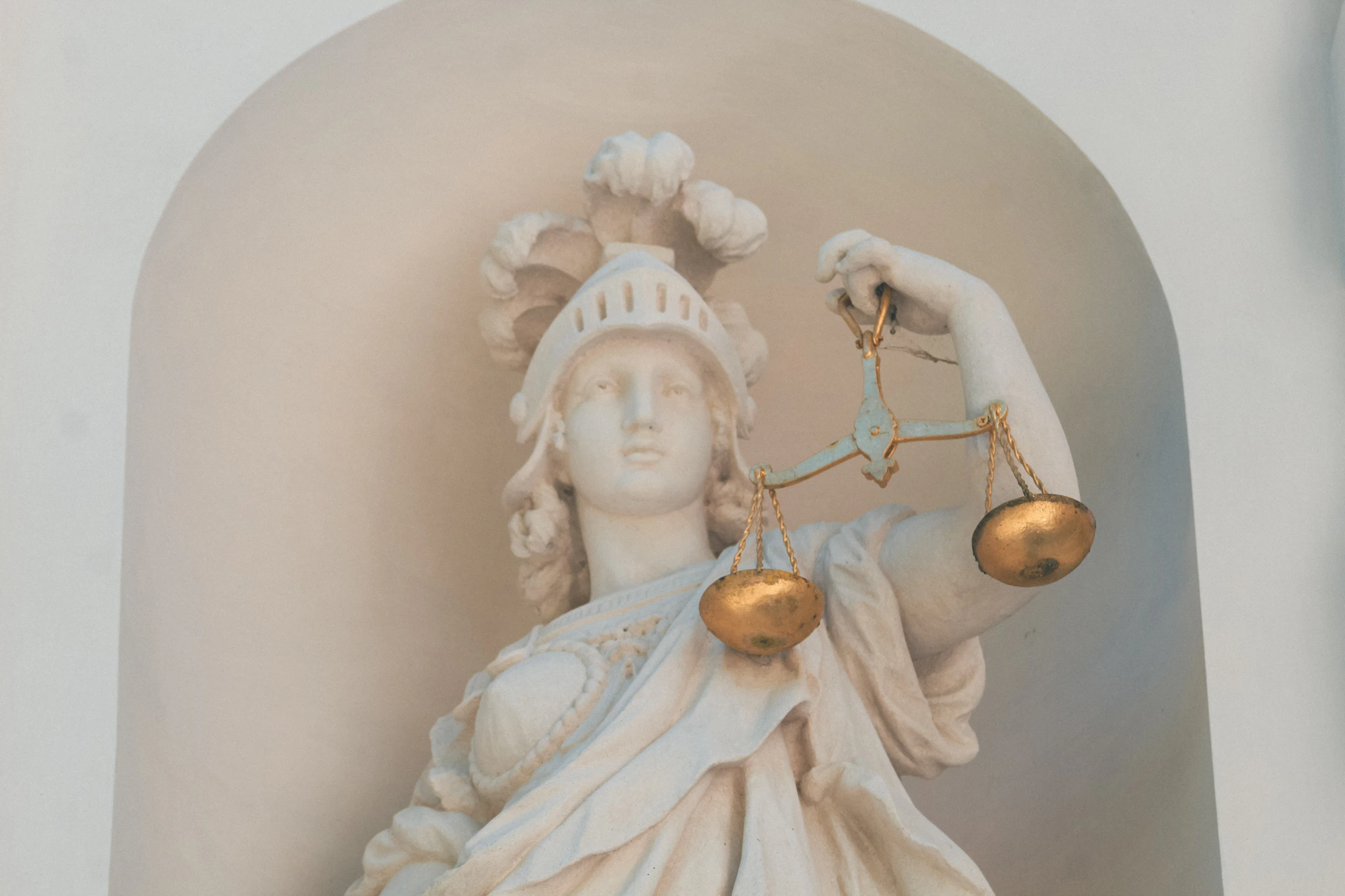 A white marble statue of a woman in a helmet holding golden scales