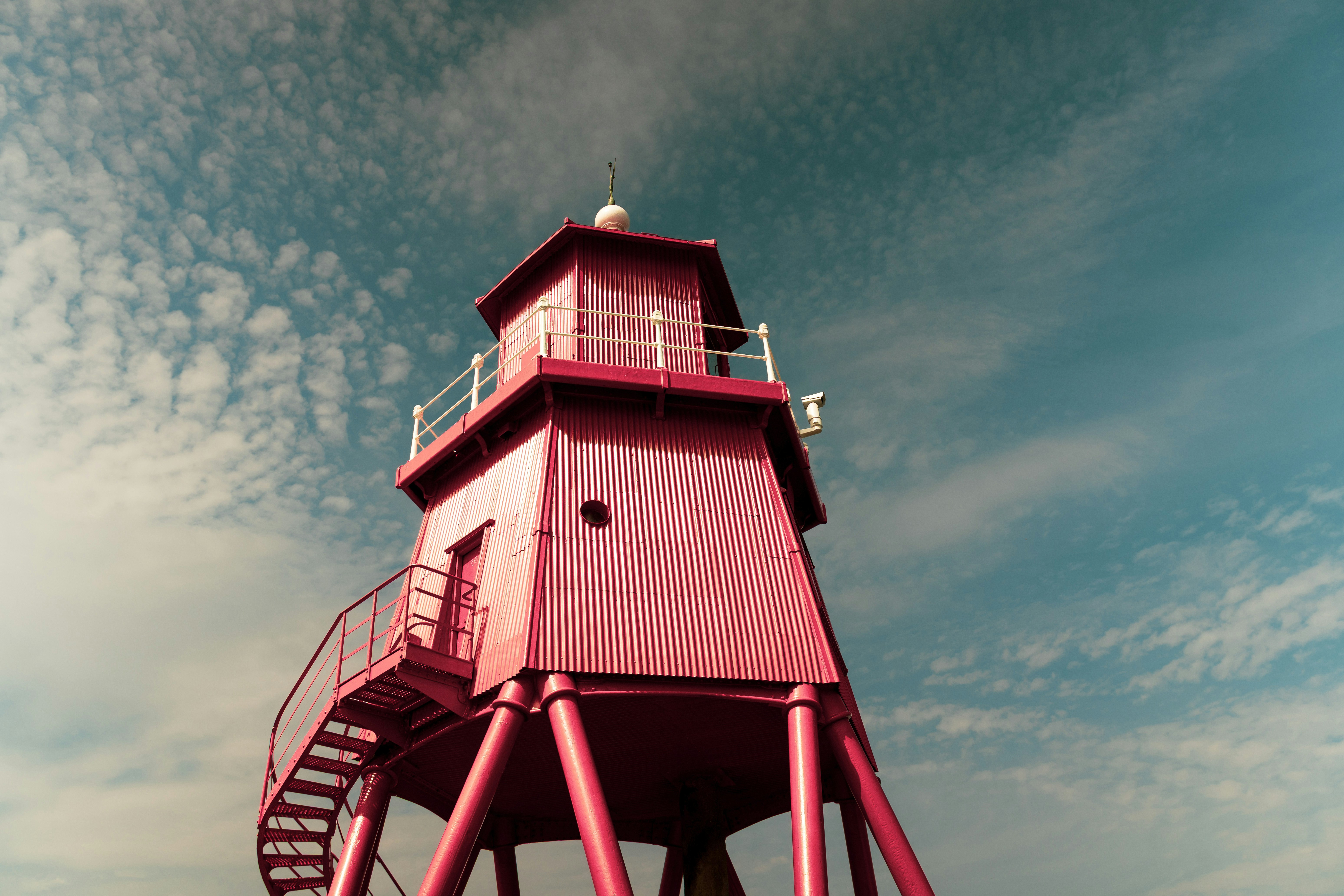 A bright pink lighthouse with a spiral staircase against a blue sky
