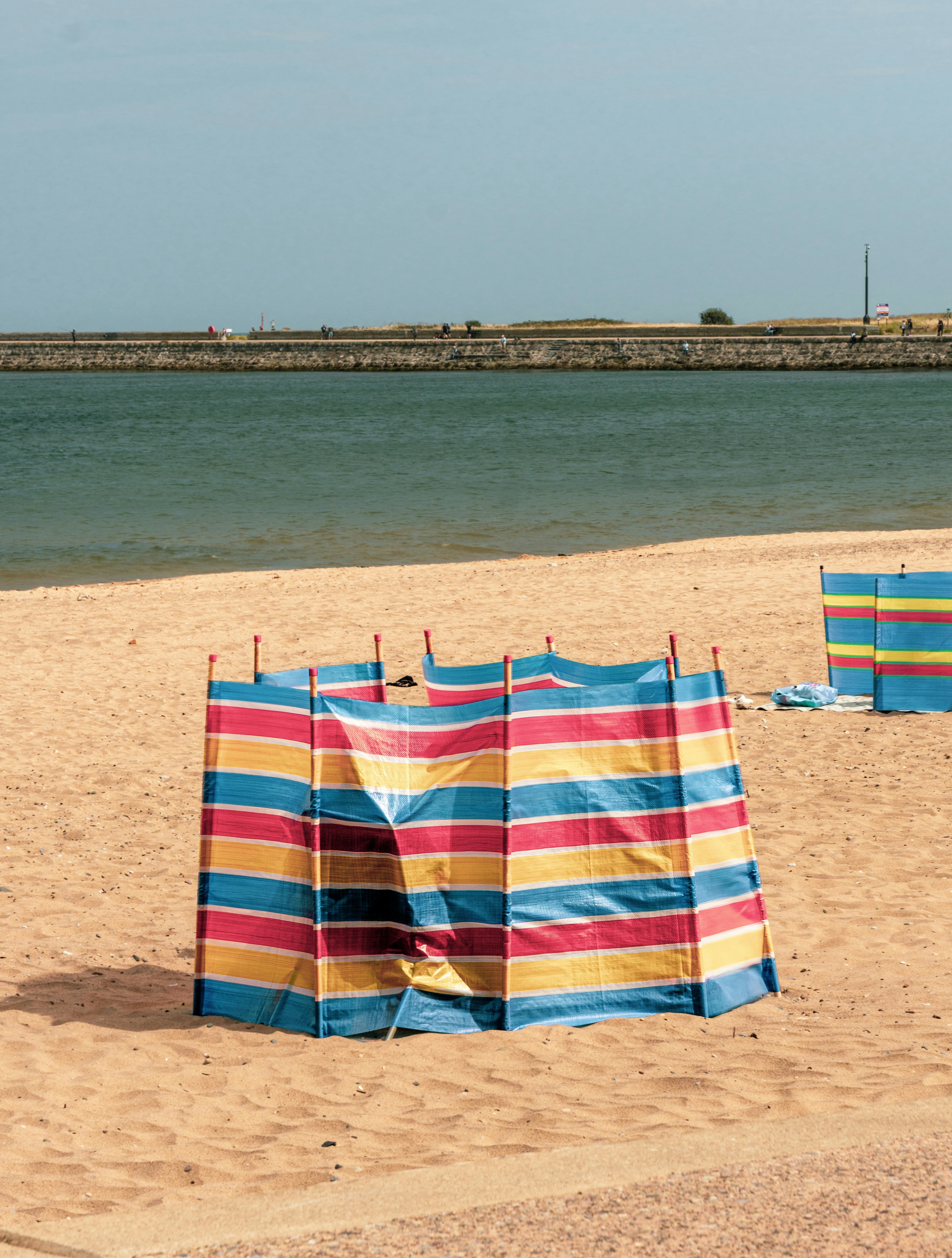 Striped windbreaks on a sandy beach with a stone seawall and water behind