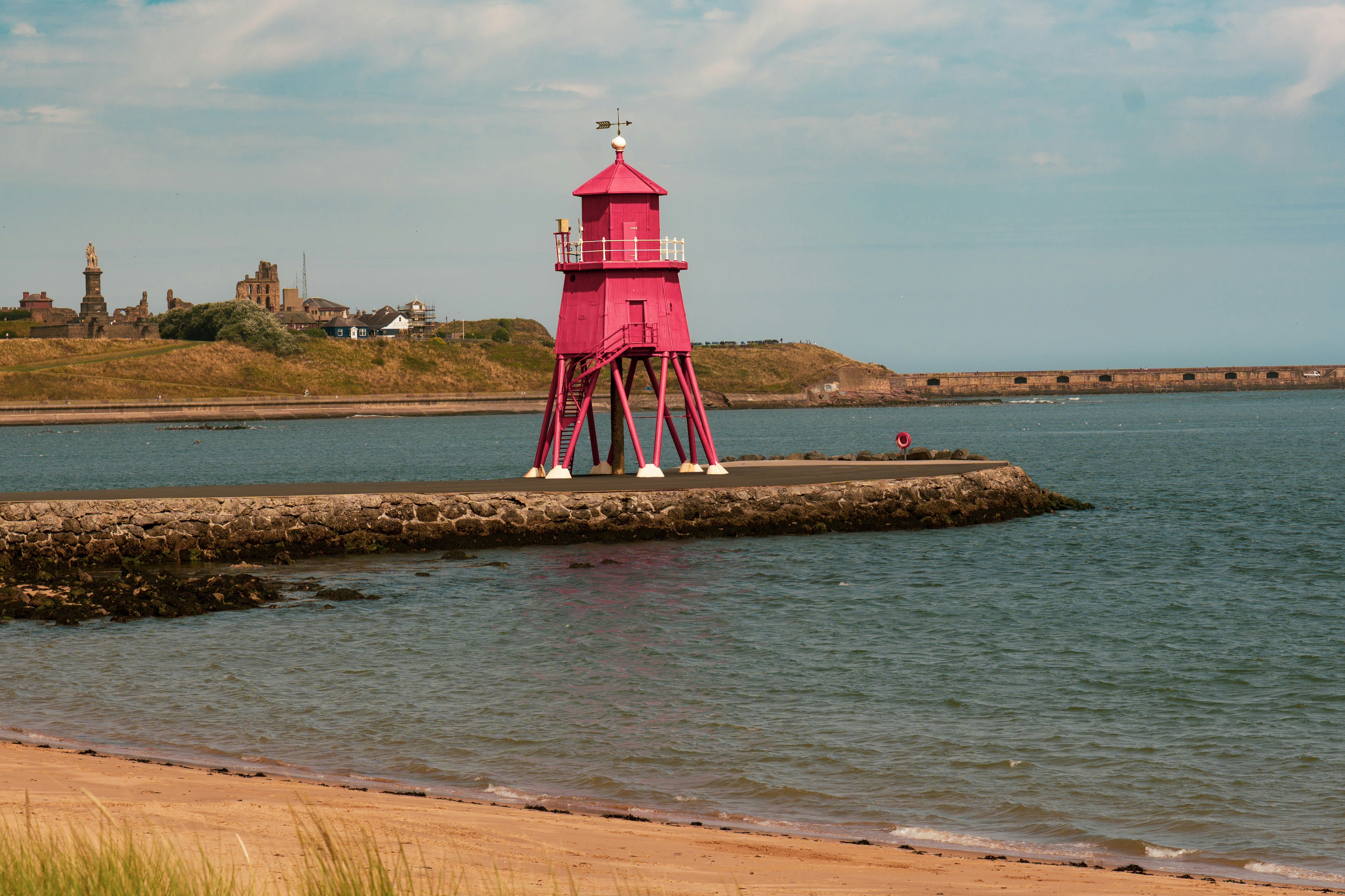 A bright pink lighthouse on a stone pier extending into the sea