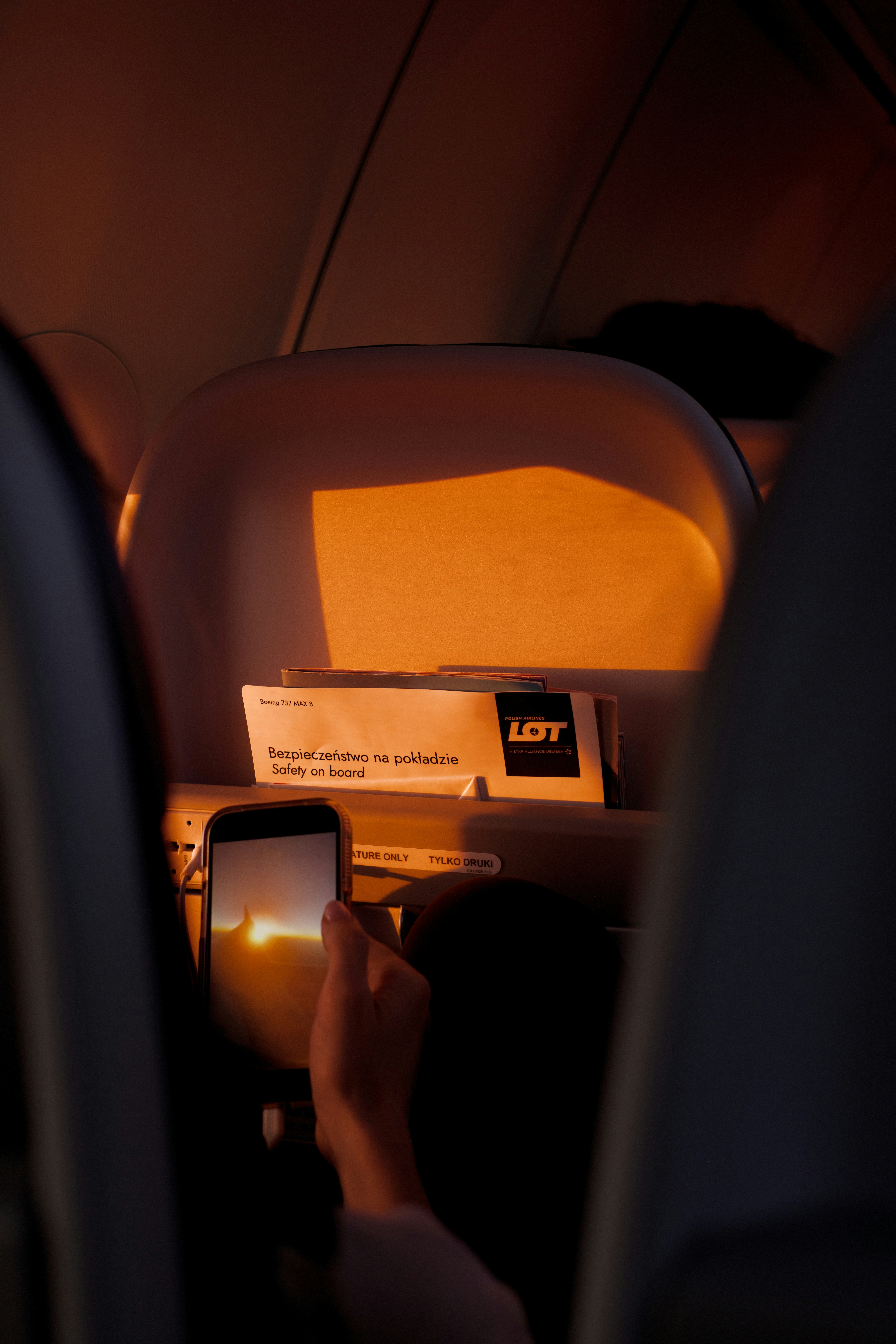 A passenger holds up a smartphone to photograph the sunset through an airplane window