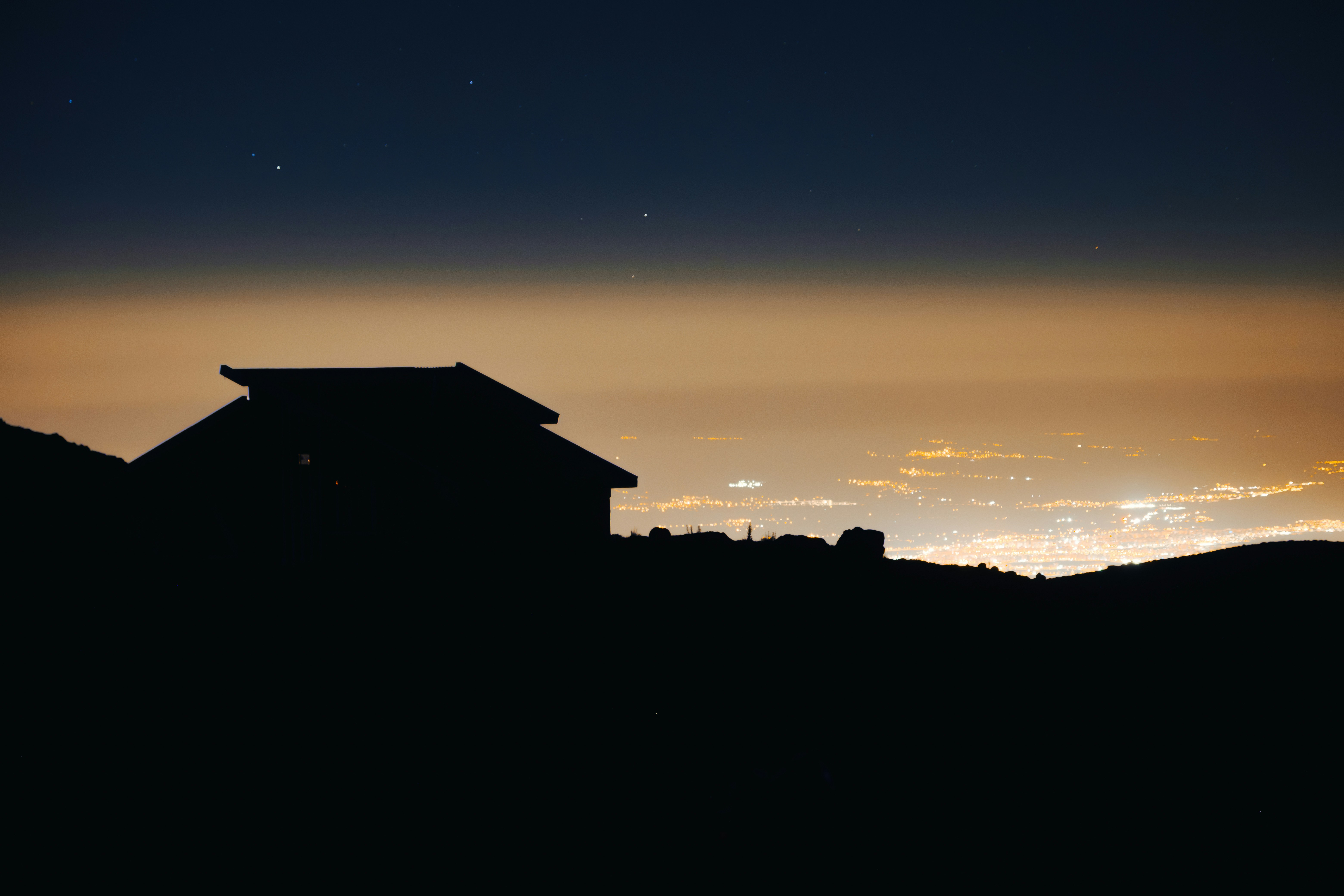A silhouette of a building on a ridge overlooking a glowing city at night