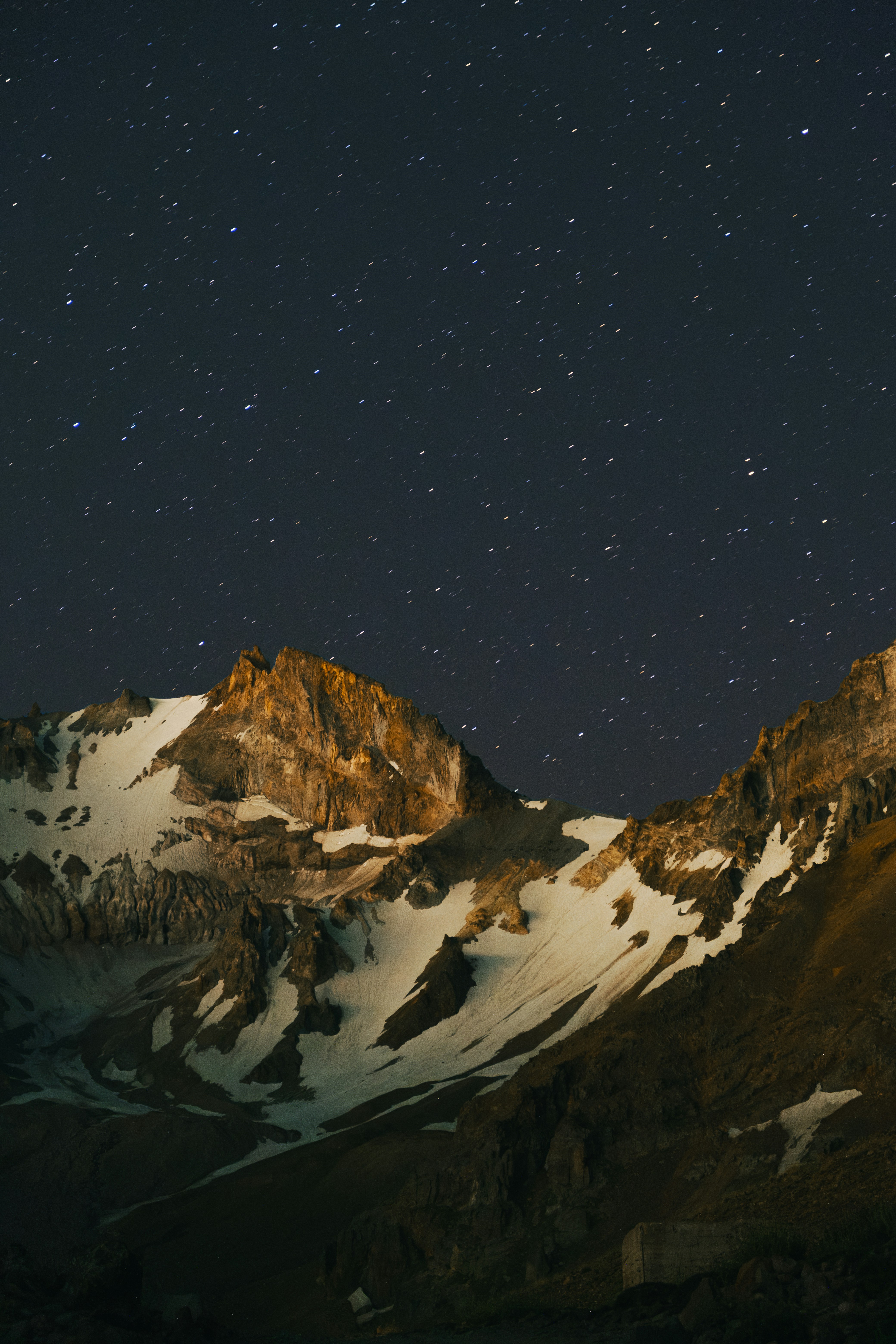 Snow-capped mountain peaks under a dark night sky filled with scattered stars