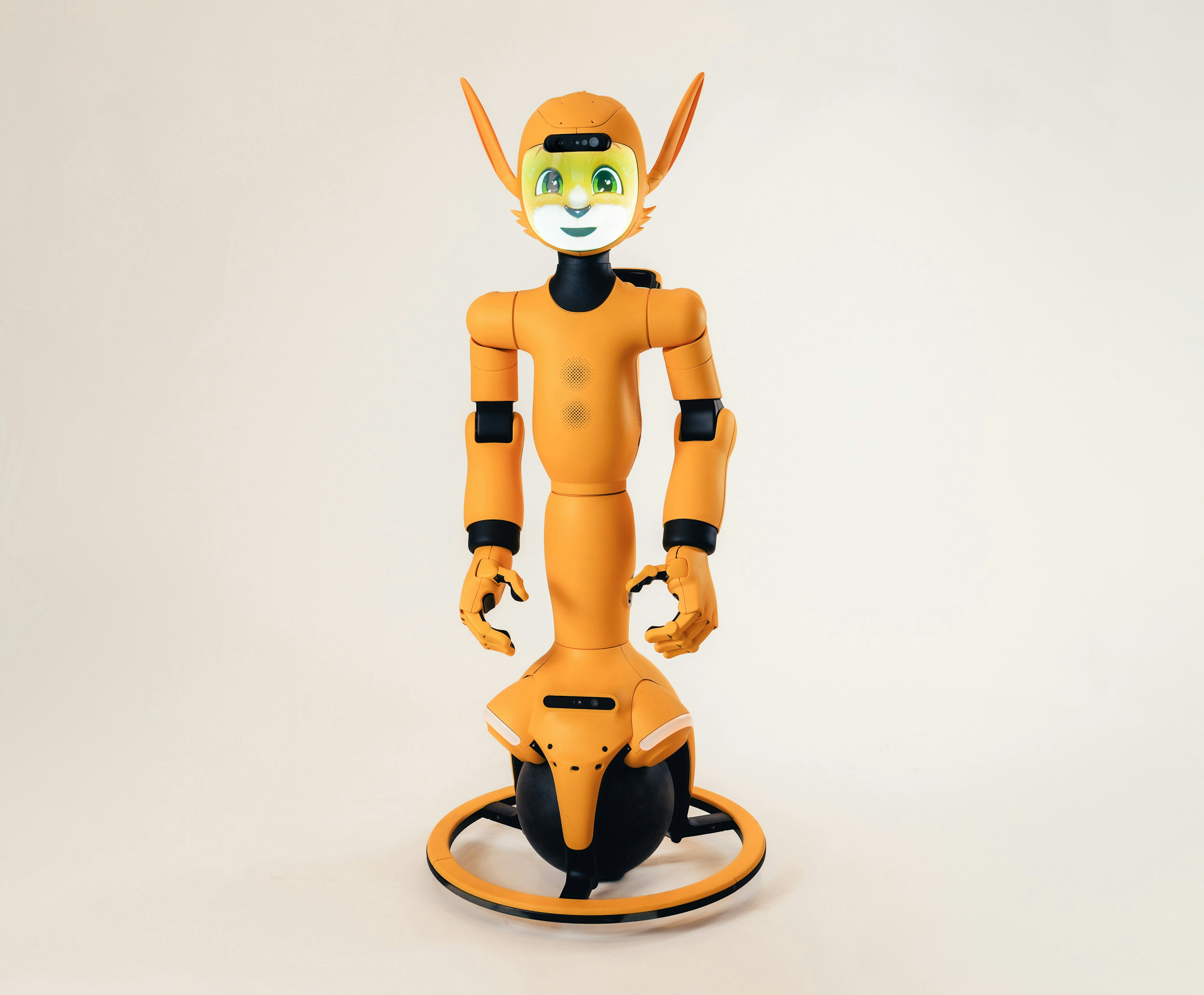 An orange humanoid robot with a digital face balancing on a black sphere