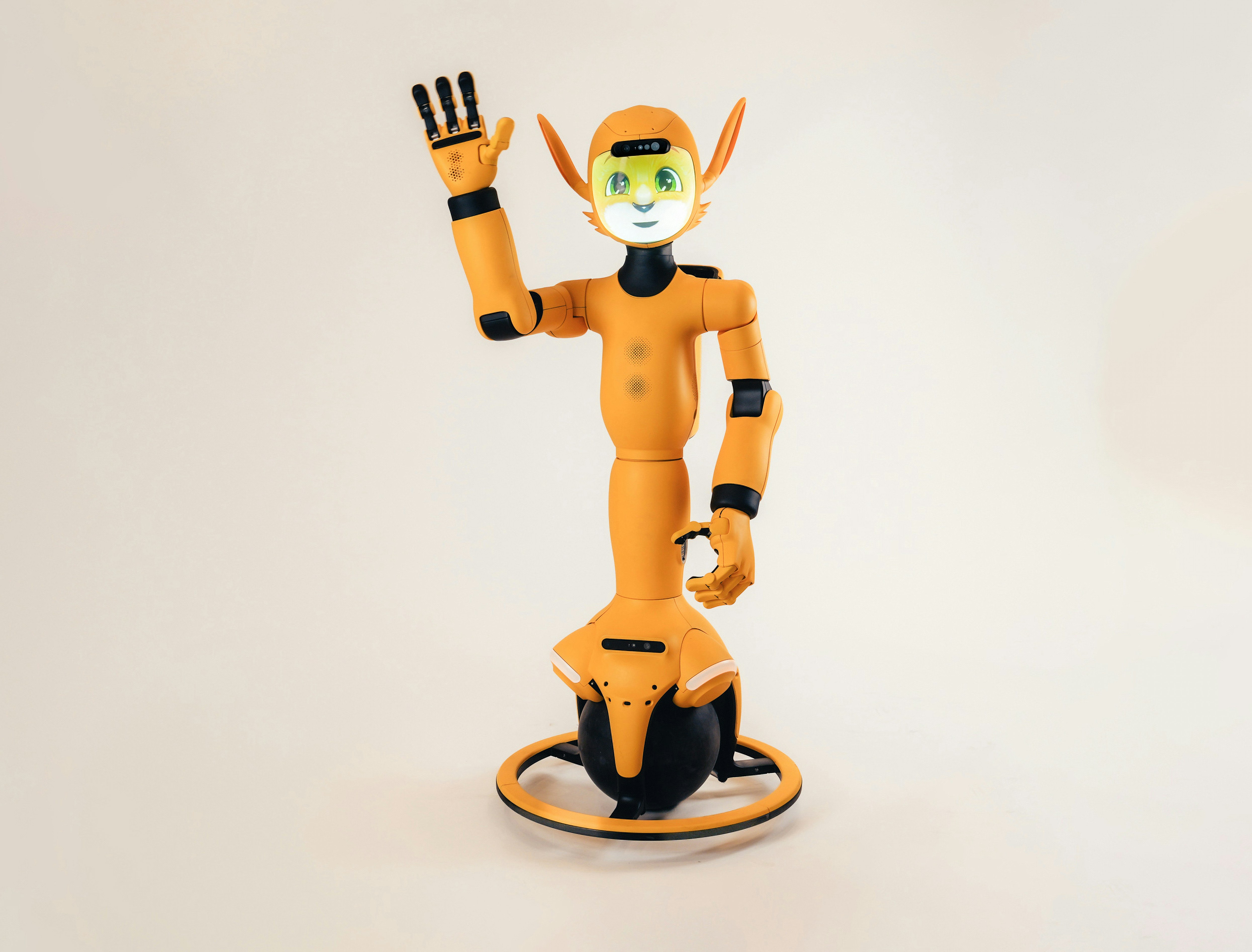 An orange humanoid robot with a digital face waving on a spherical base