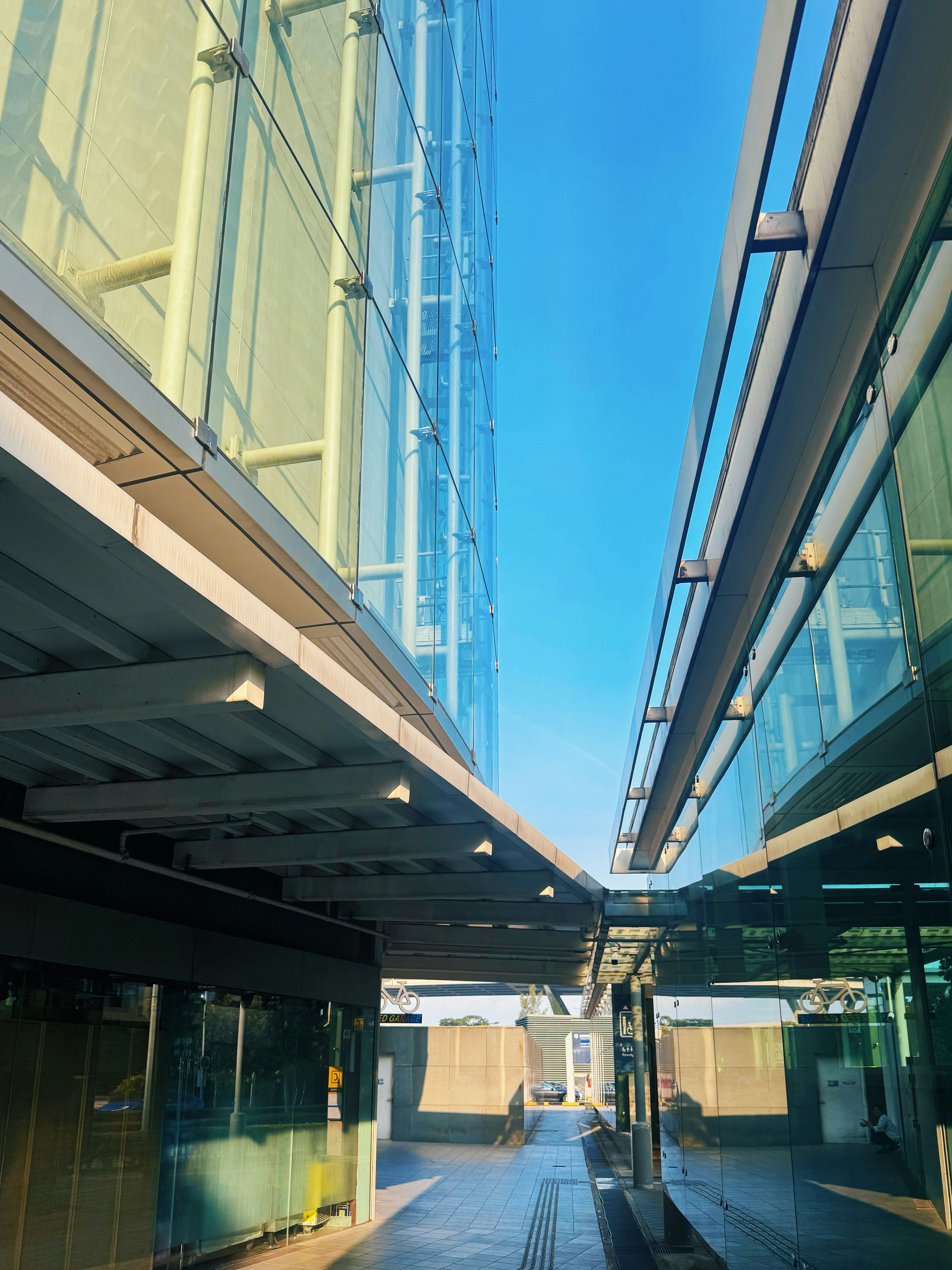 A narrow walkway between two modern glass buildings under a clear blue sky