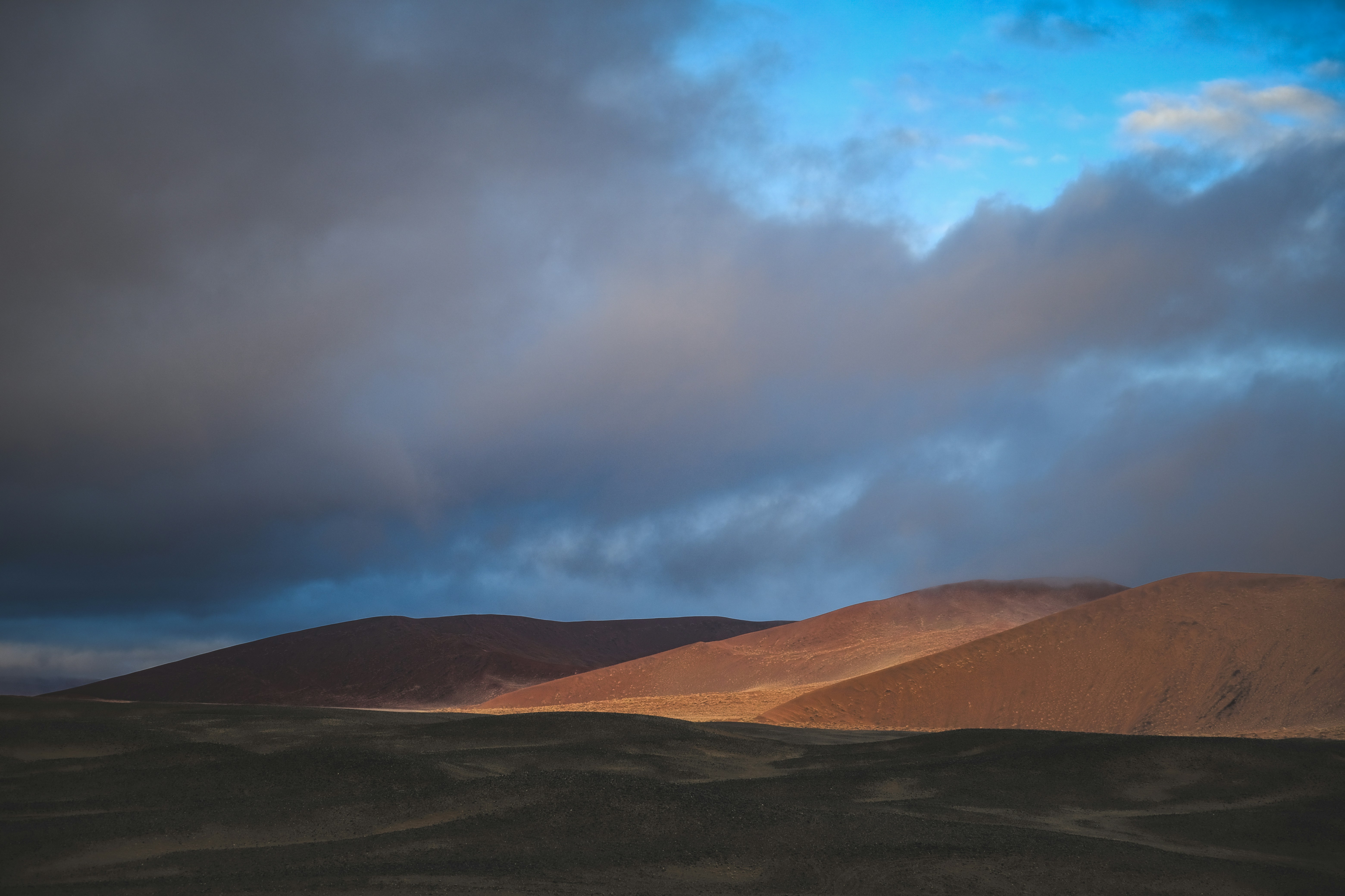 Reddish brown desert hills under a dark cloudy sky at low sun