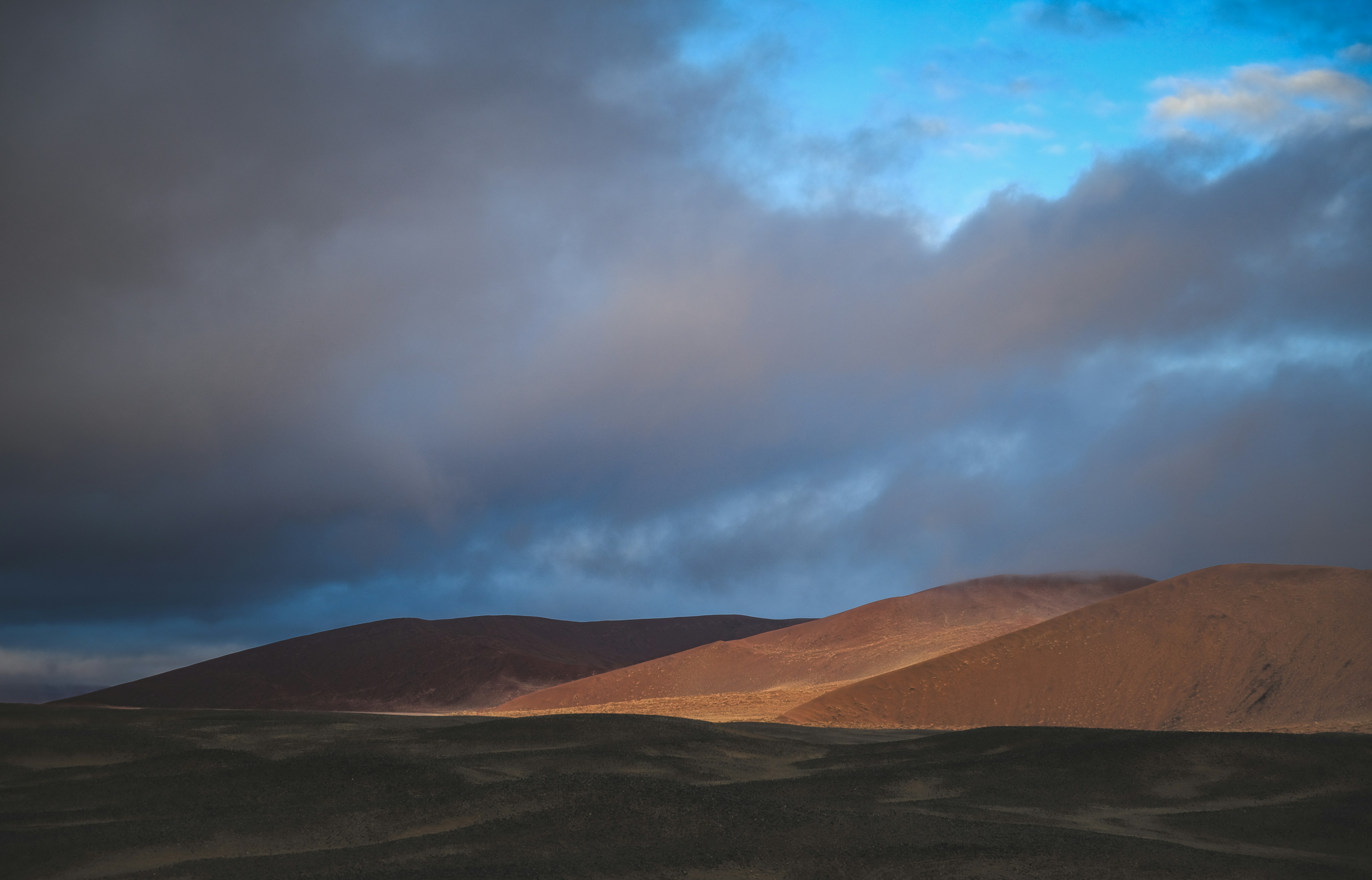 Brown desert hills under a dramatic sky with dark blue and grey clouds