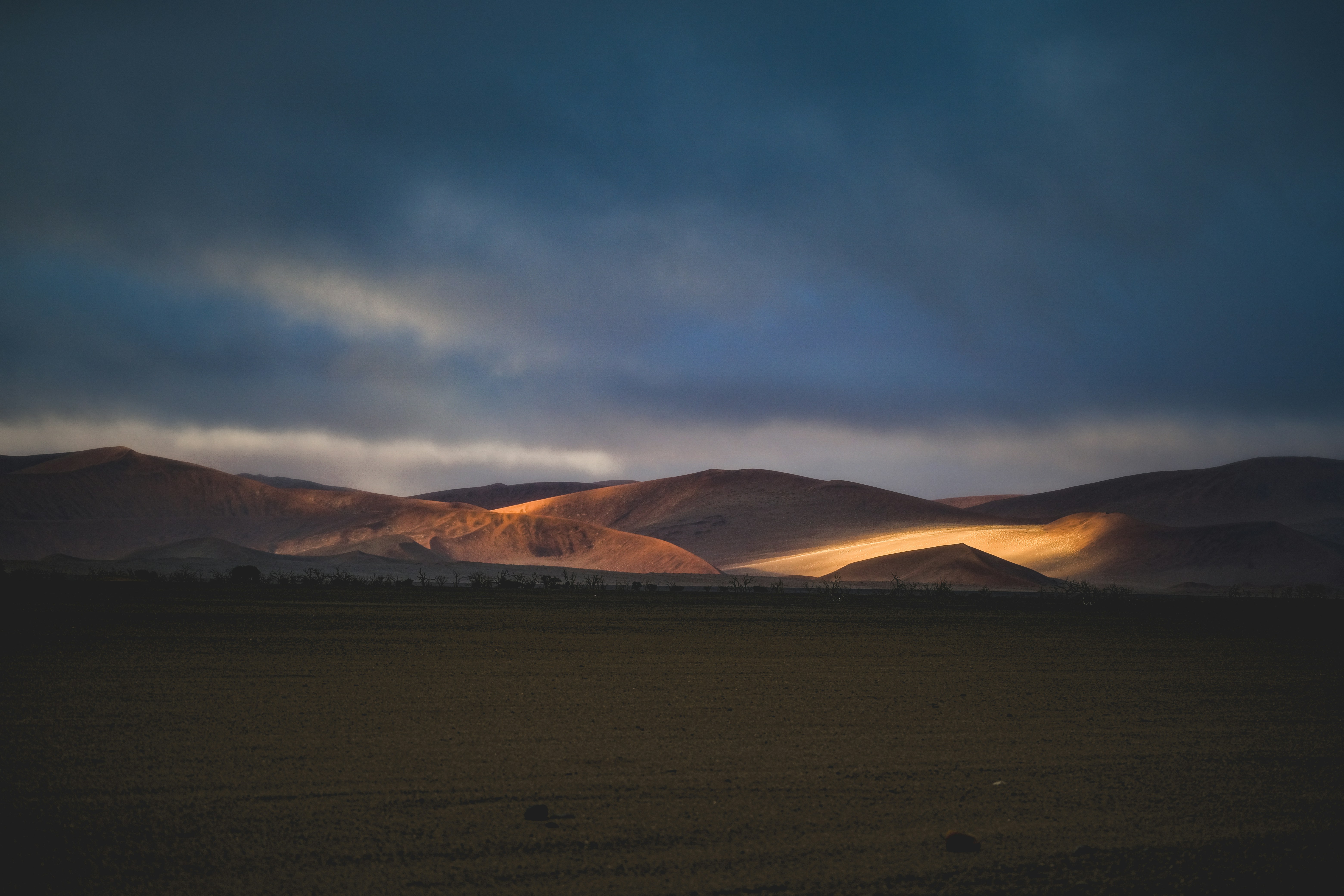 Low sun illuminating desert hills against a dark and cloudy sky