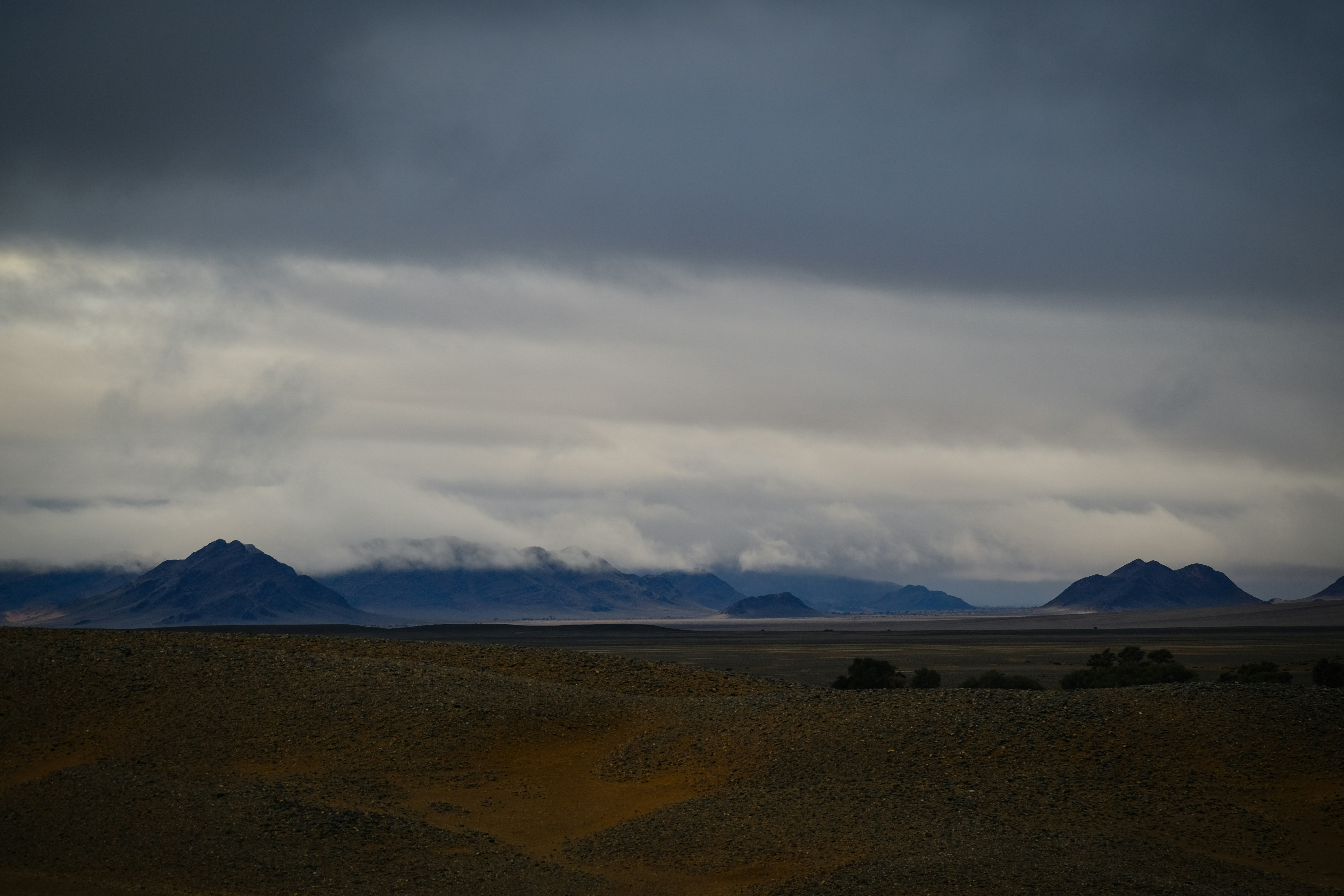 Dark mountains under a heavy overcast sky above a vast desert plain