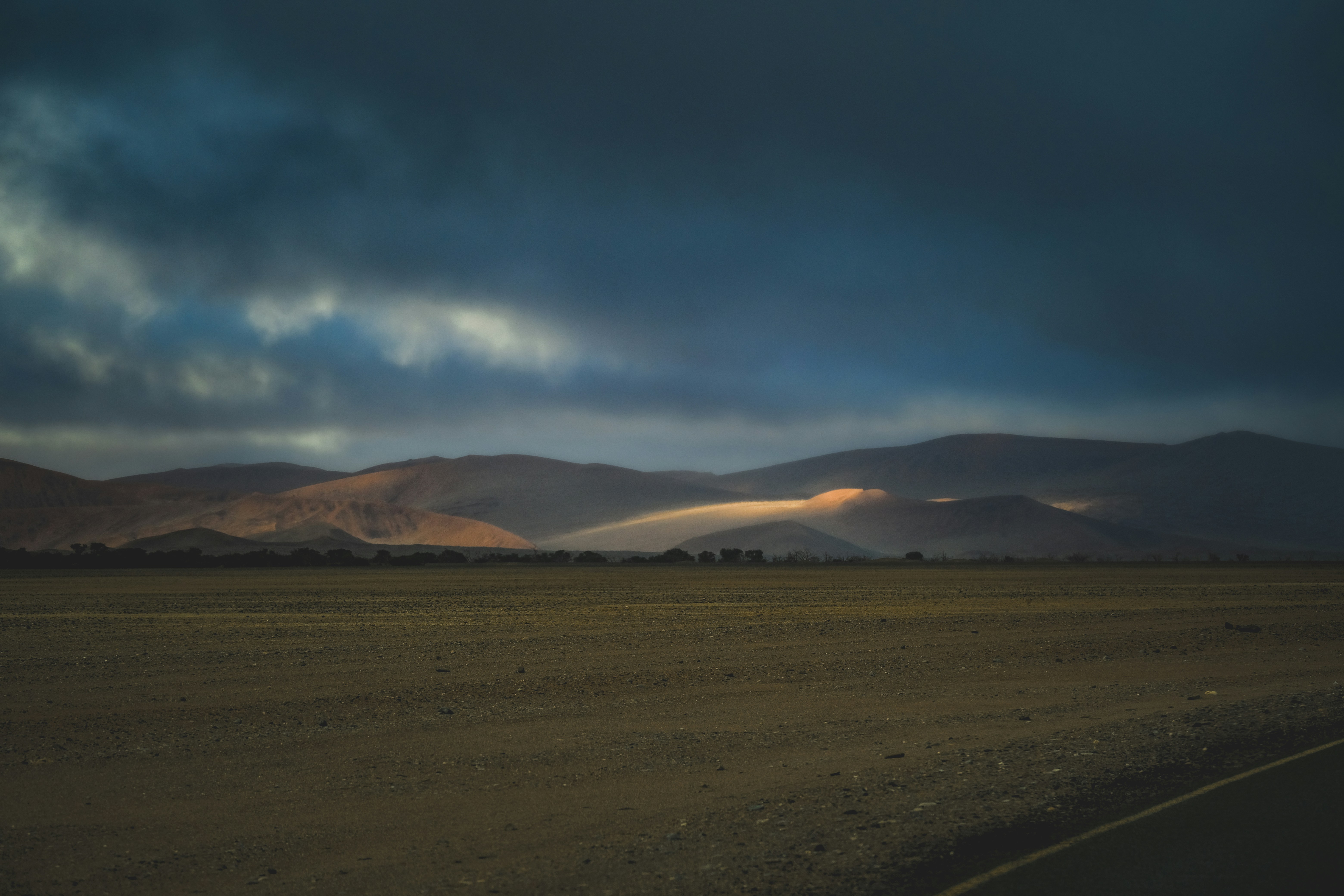 A beam of light illuminating desert mountains under a dark cloudy sky