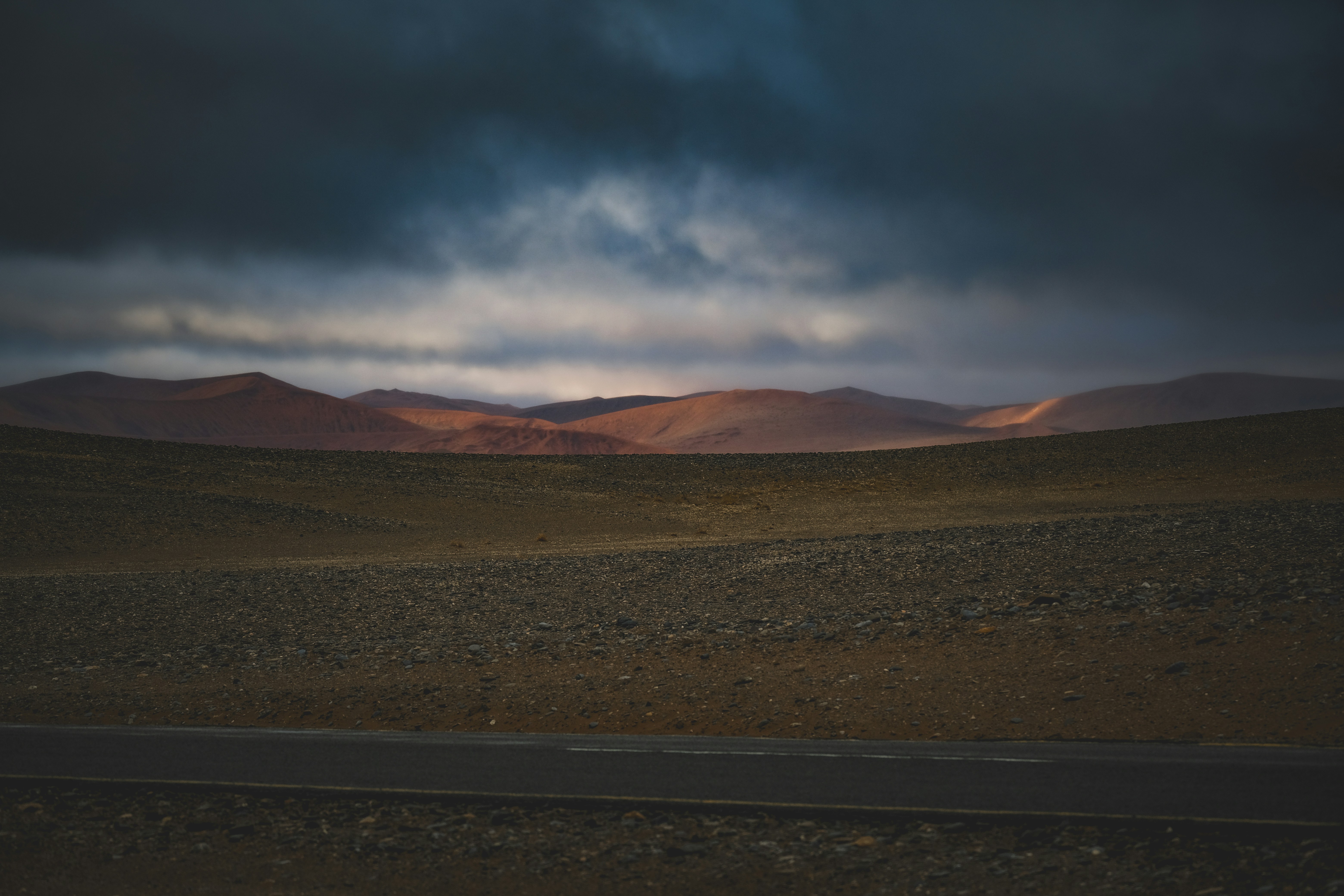 A paved road through a vast desert landscape under a dark cloudy sky