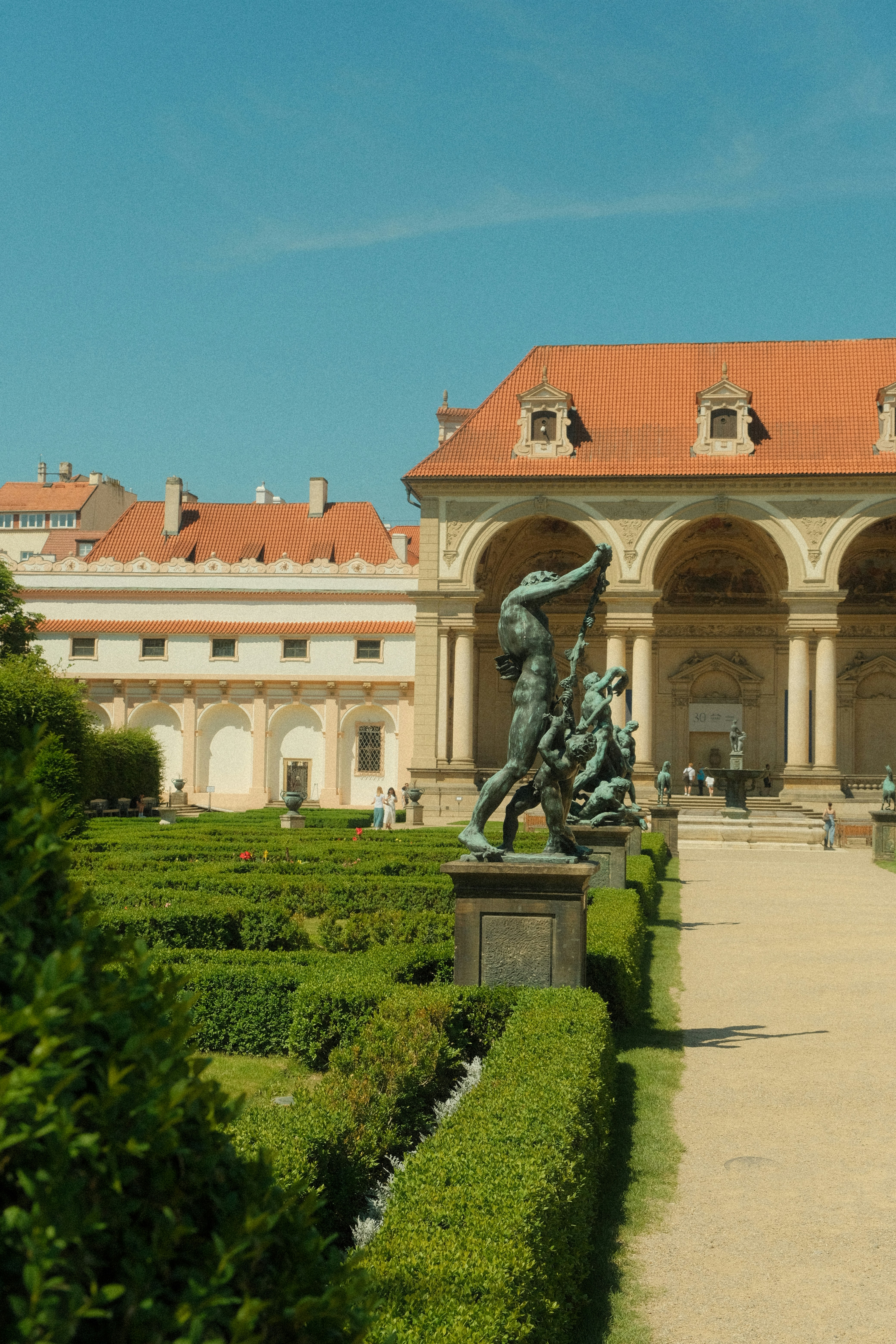 Bronze statues in a manicured garden with a historic building in Prague