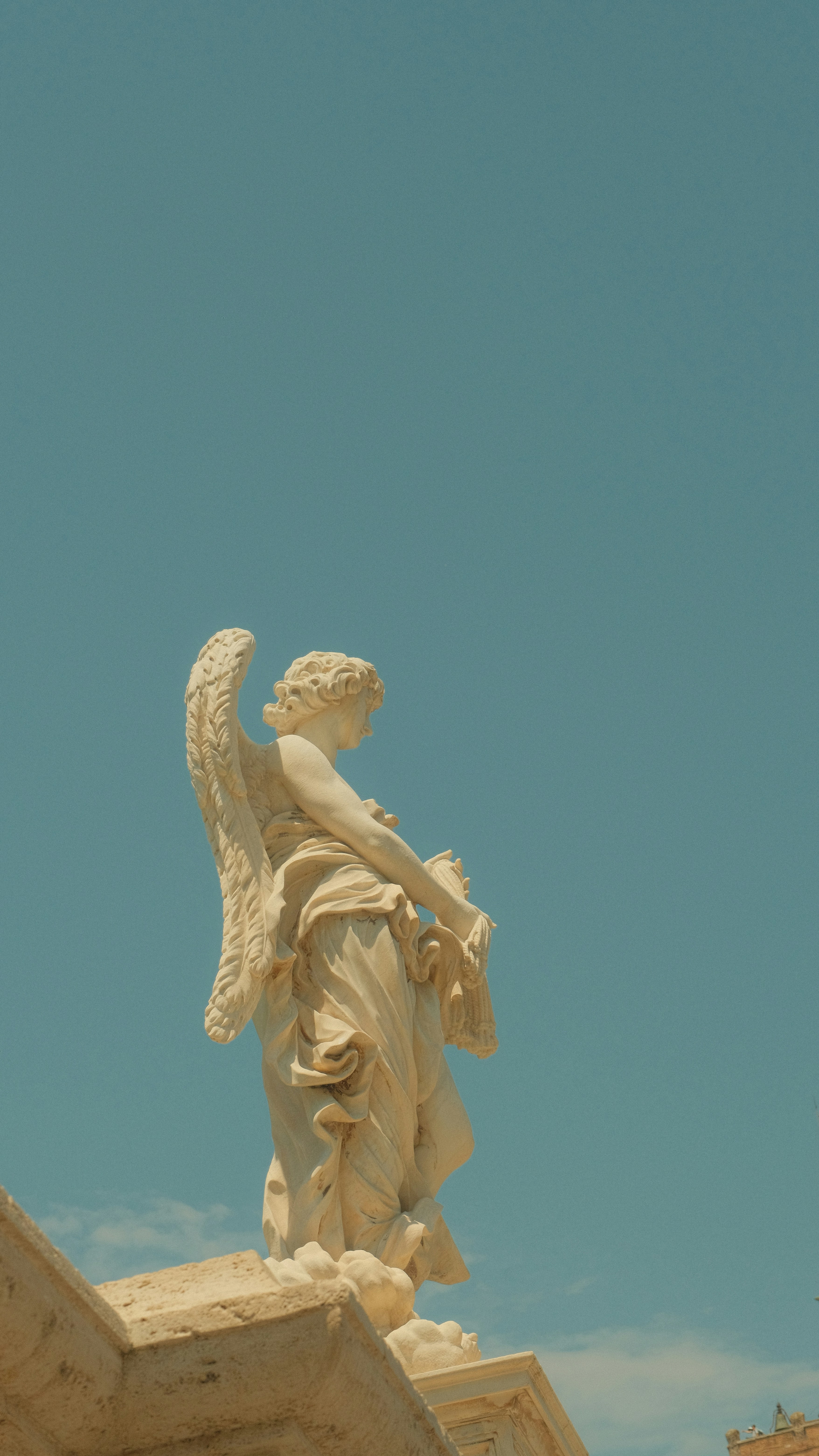A stone angel statue with feathered wings against a clear blue sky