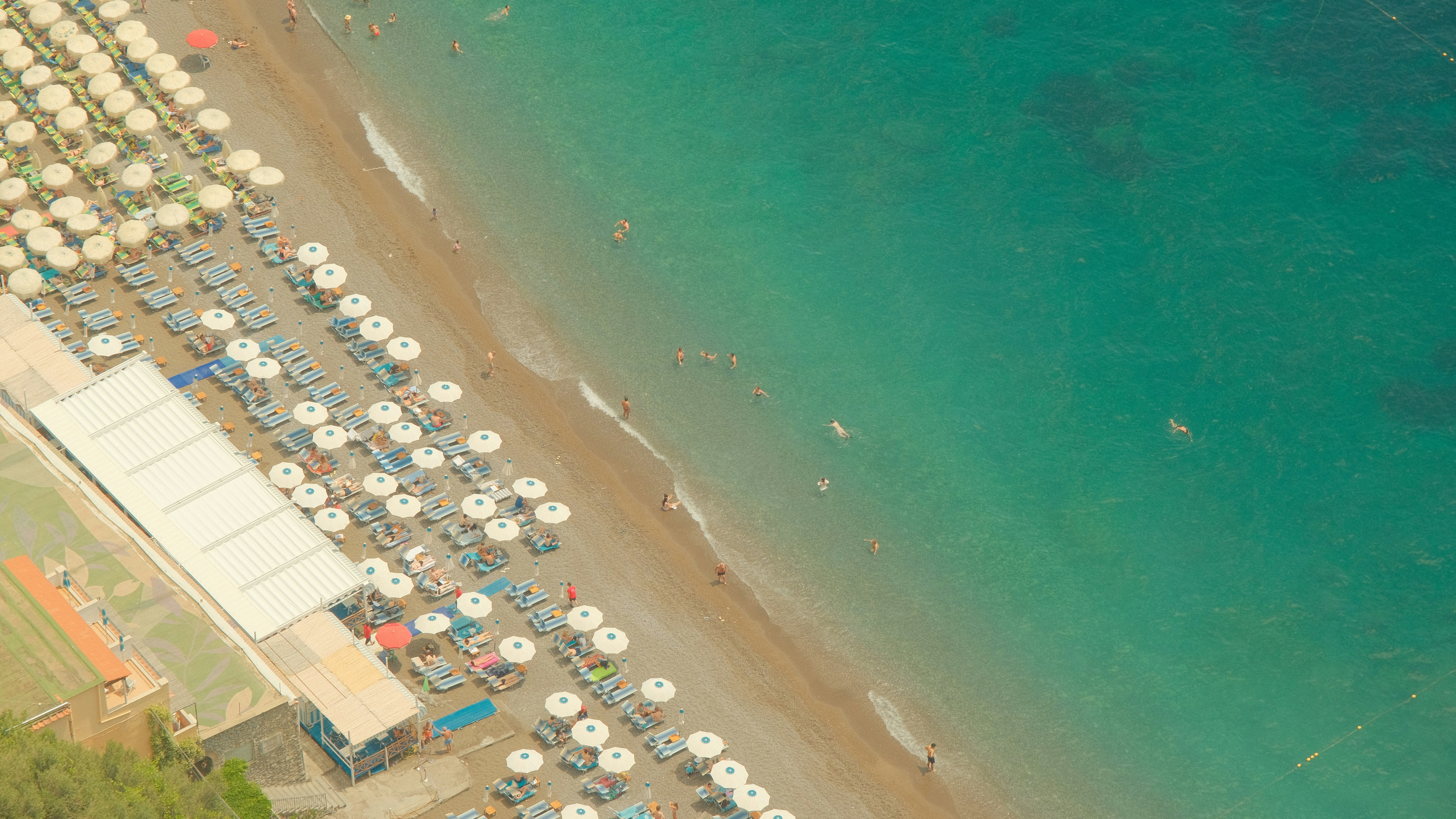 An aerial view of a sandy beach with rows of white umbrellas and people swimming