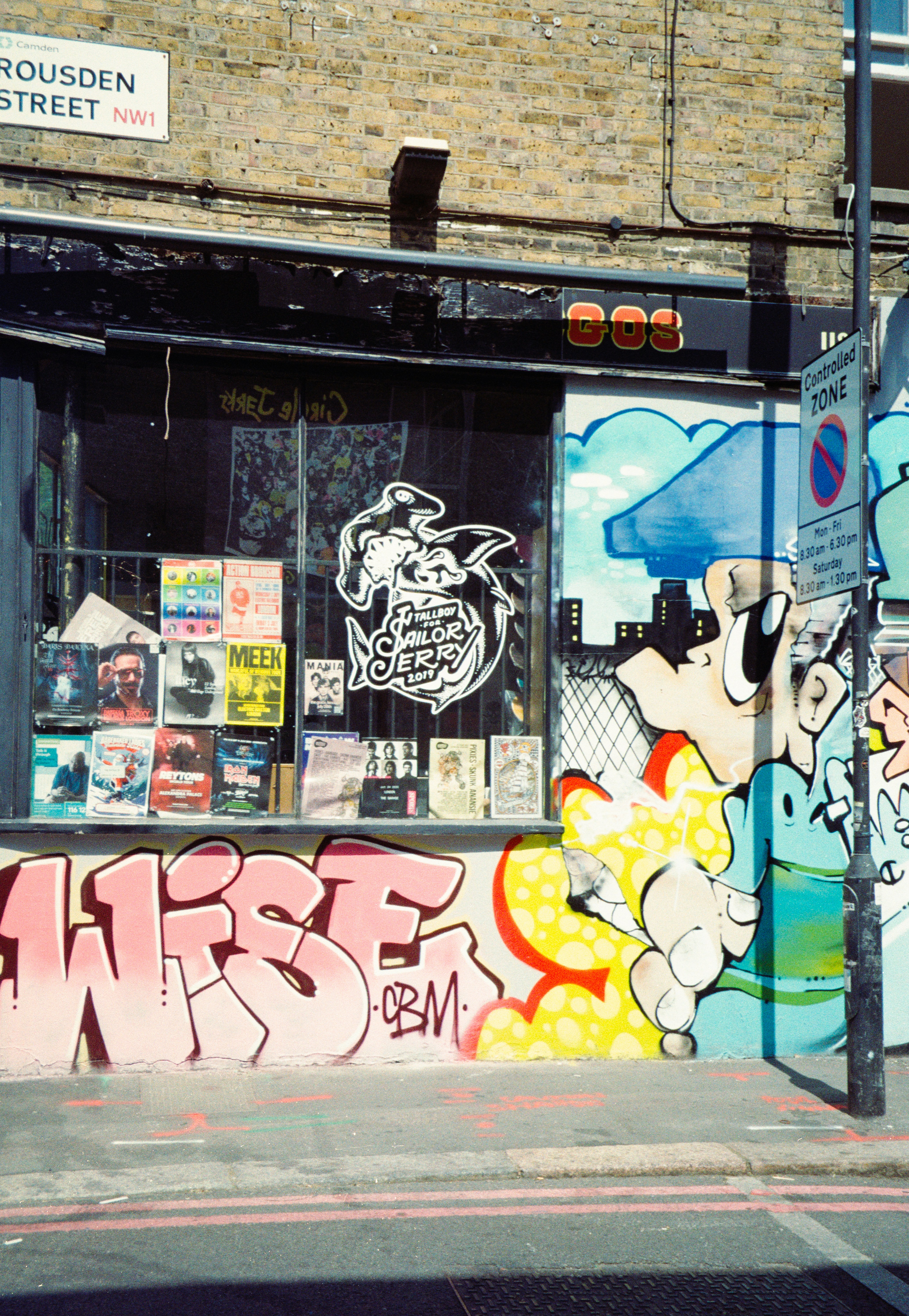 A brick storefront covered in colorful graffiti with posters displayed in the window