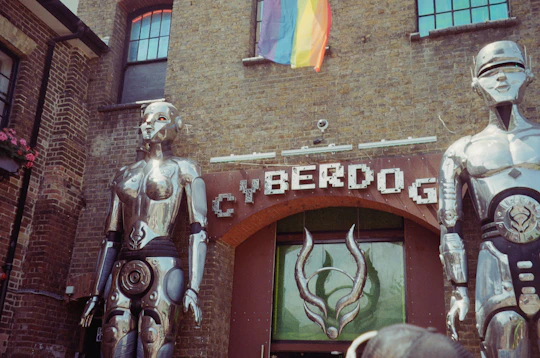 Two silver robot statues at a store entrance reading "CYBERDOG" under a rainbow flag
