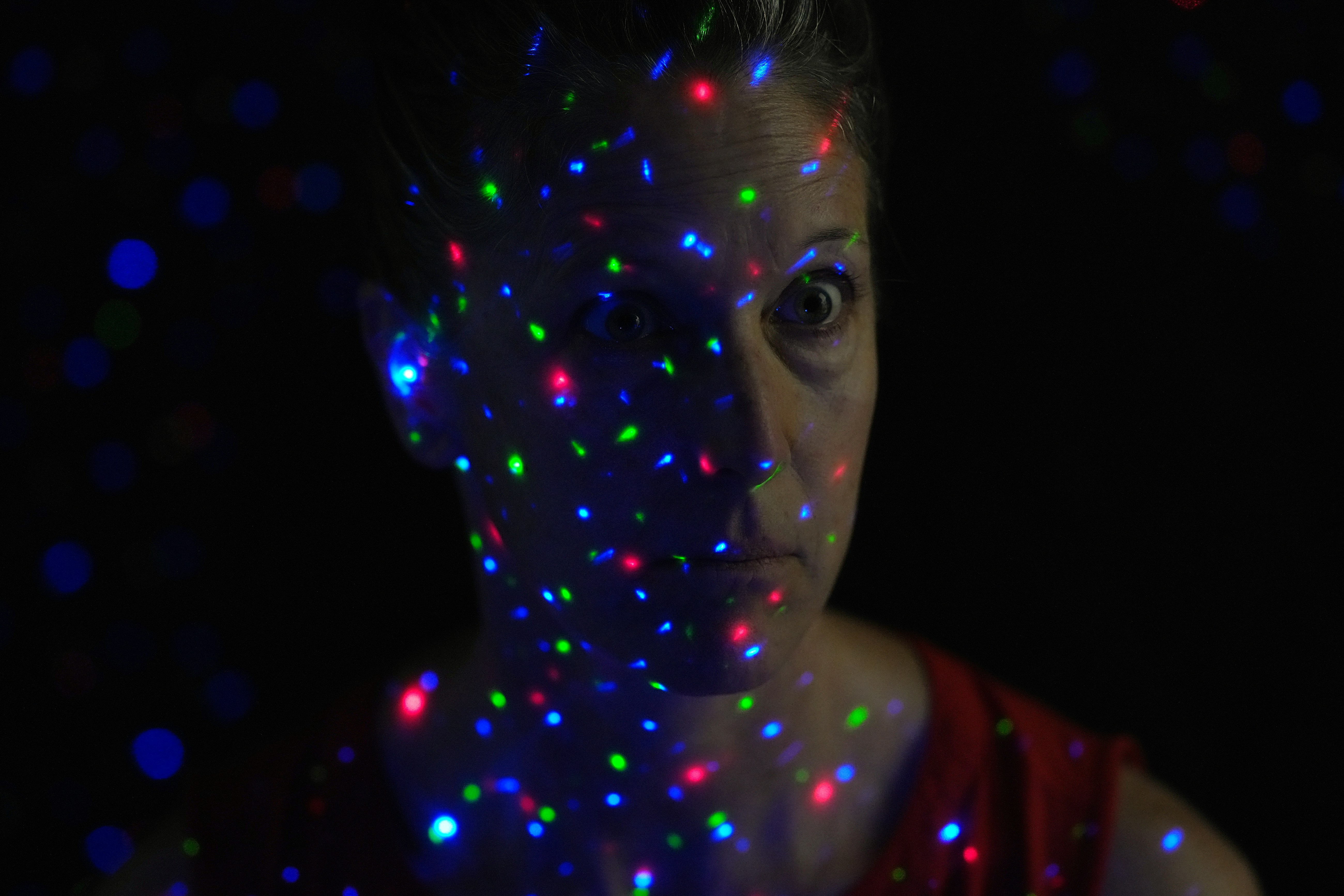 A woman in a red top illuminated by scattered red, green, and blue lights