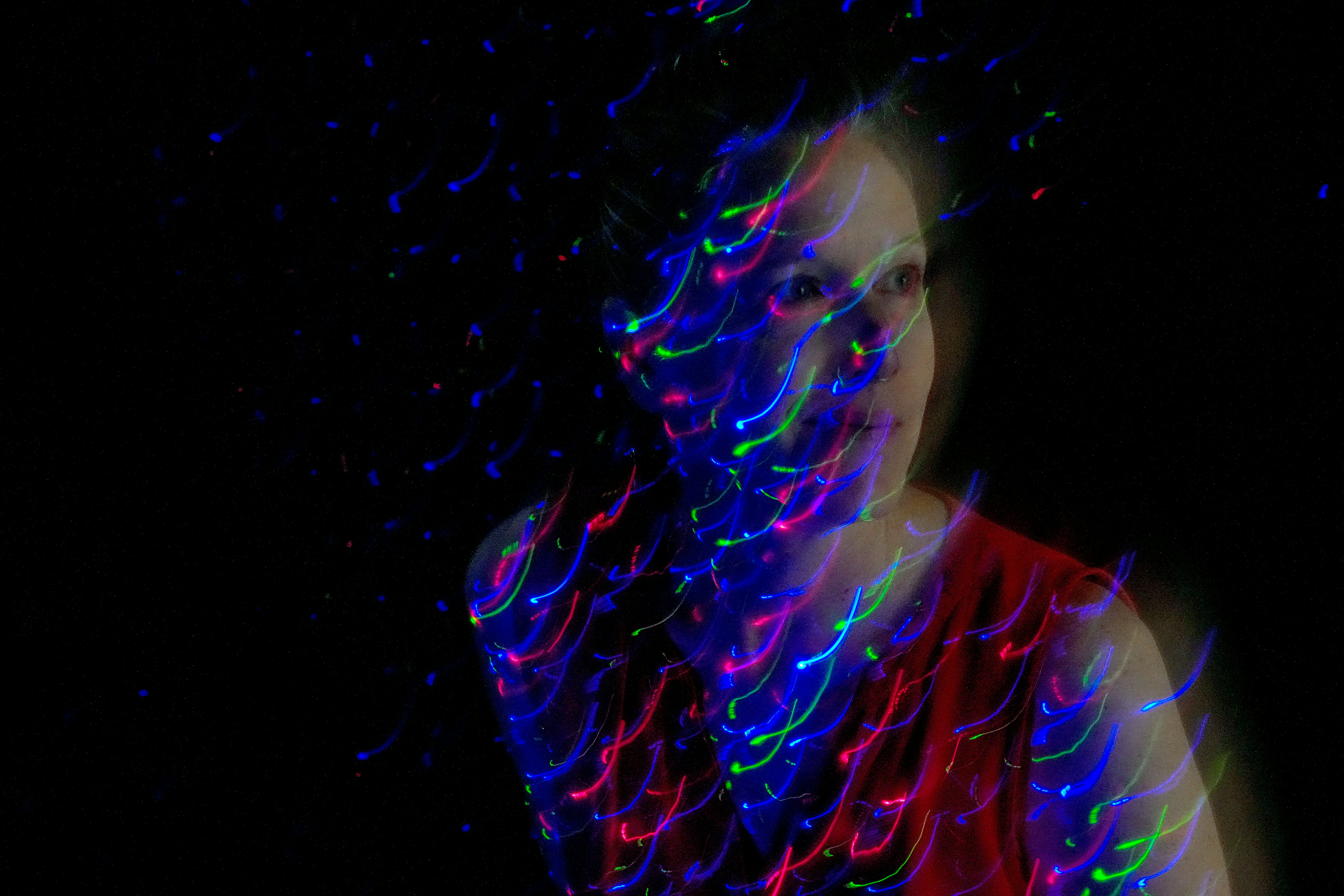 A woman in a red top illuminated by swirling red and green light trails
