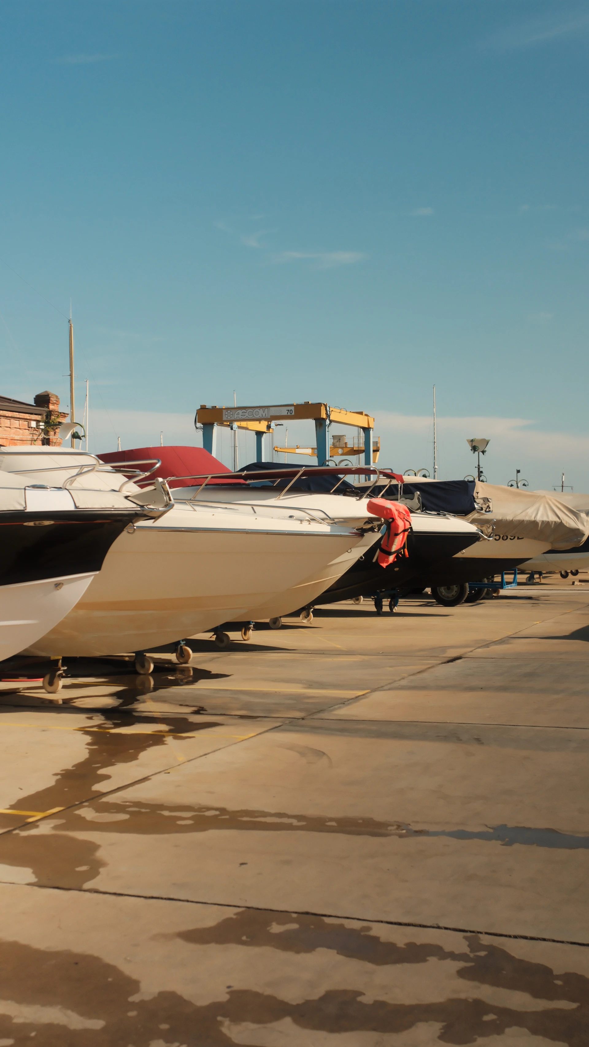 Motorboats on trailers in a paved boatyard under a clear blue sky