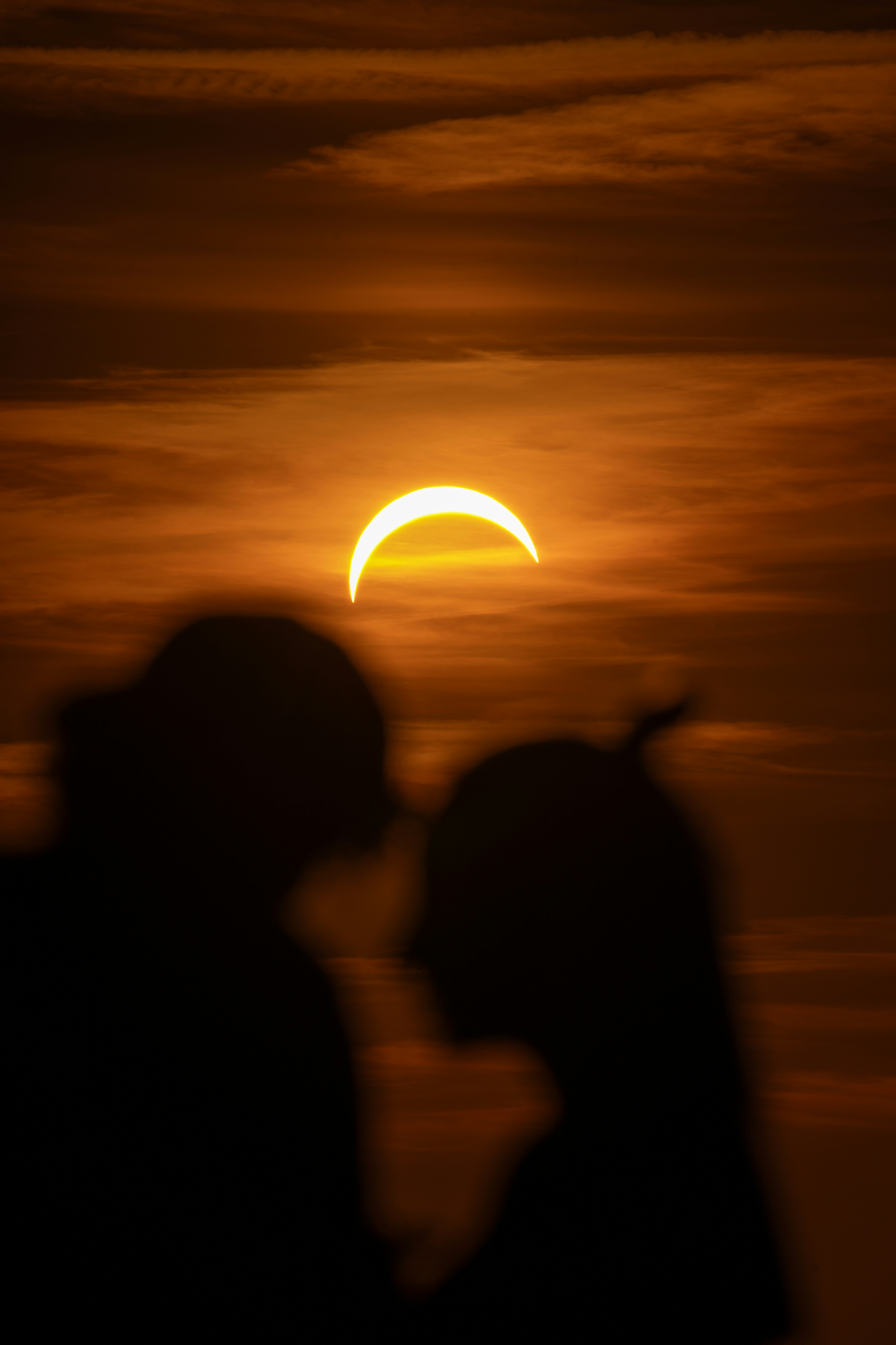 Silhouettes of two people against a partial solar eclipse in a warm orange sky