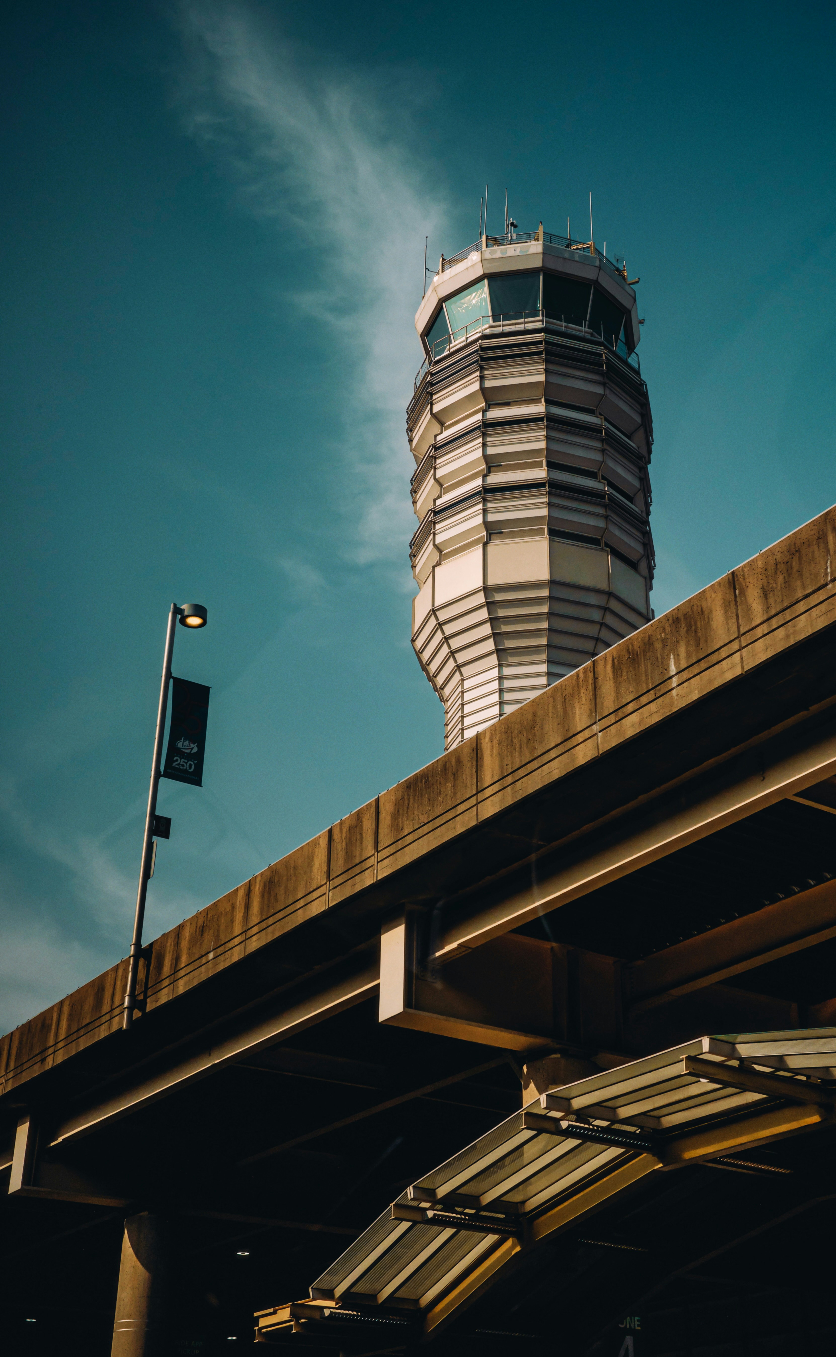 An airport control tower rising above a concrete overpass against a blue sky