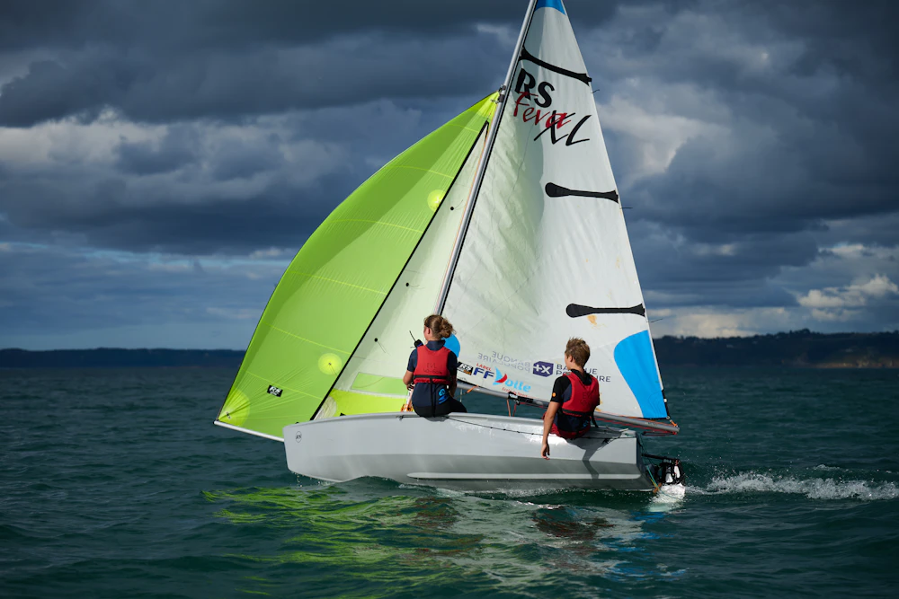 Two sailors sailing an RS Feva dinghy with a bright green spinnaker