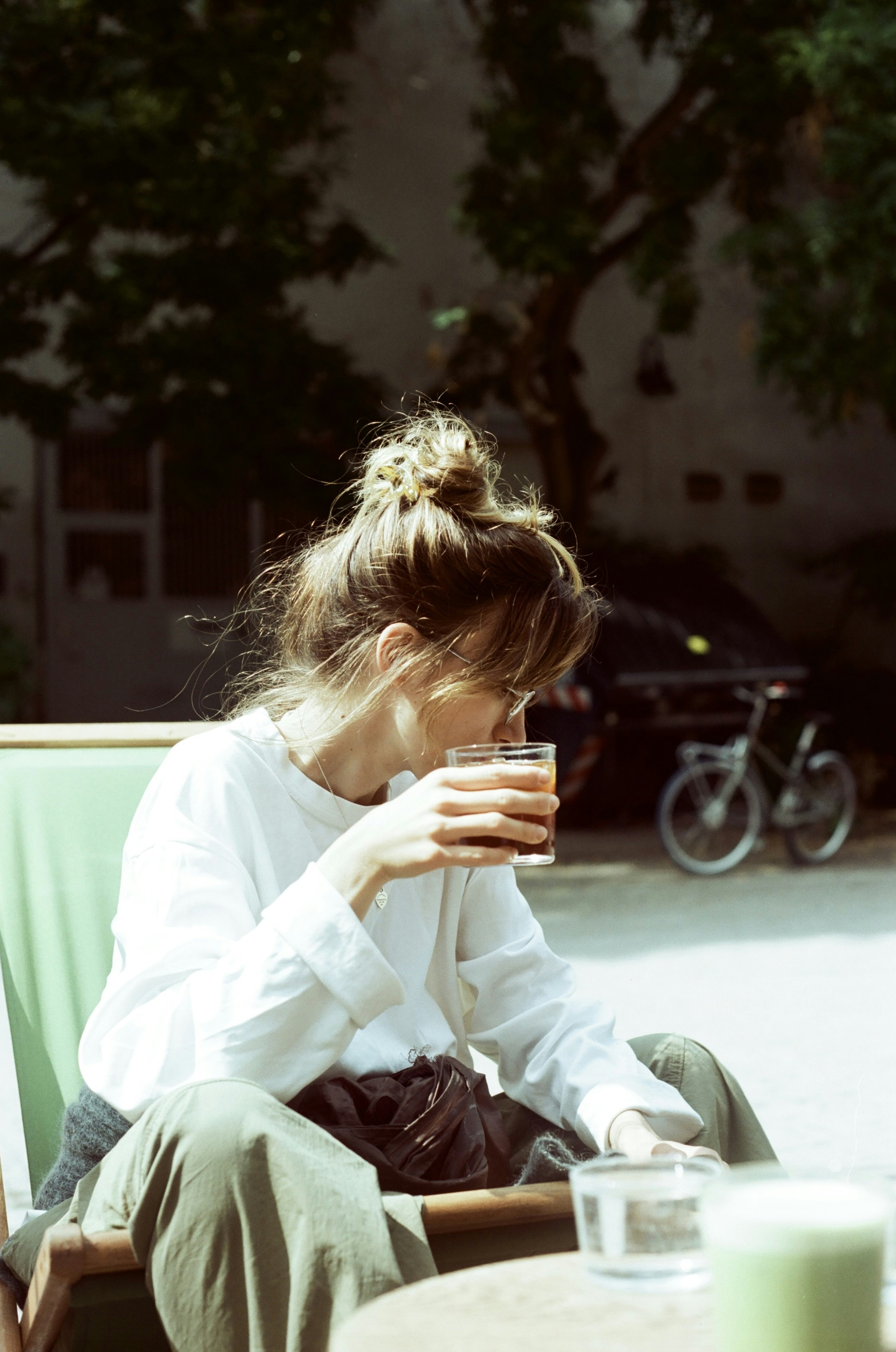 A woman with hair in a bun drinking from a glass outdoors