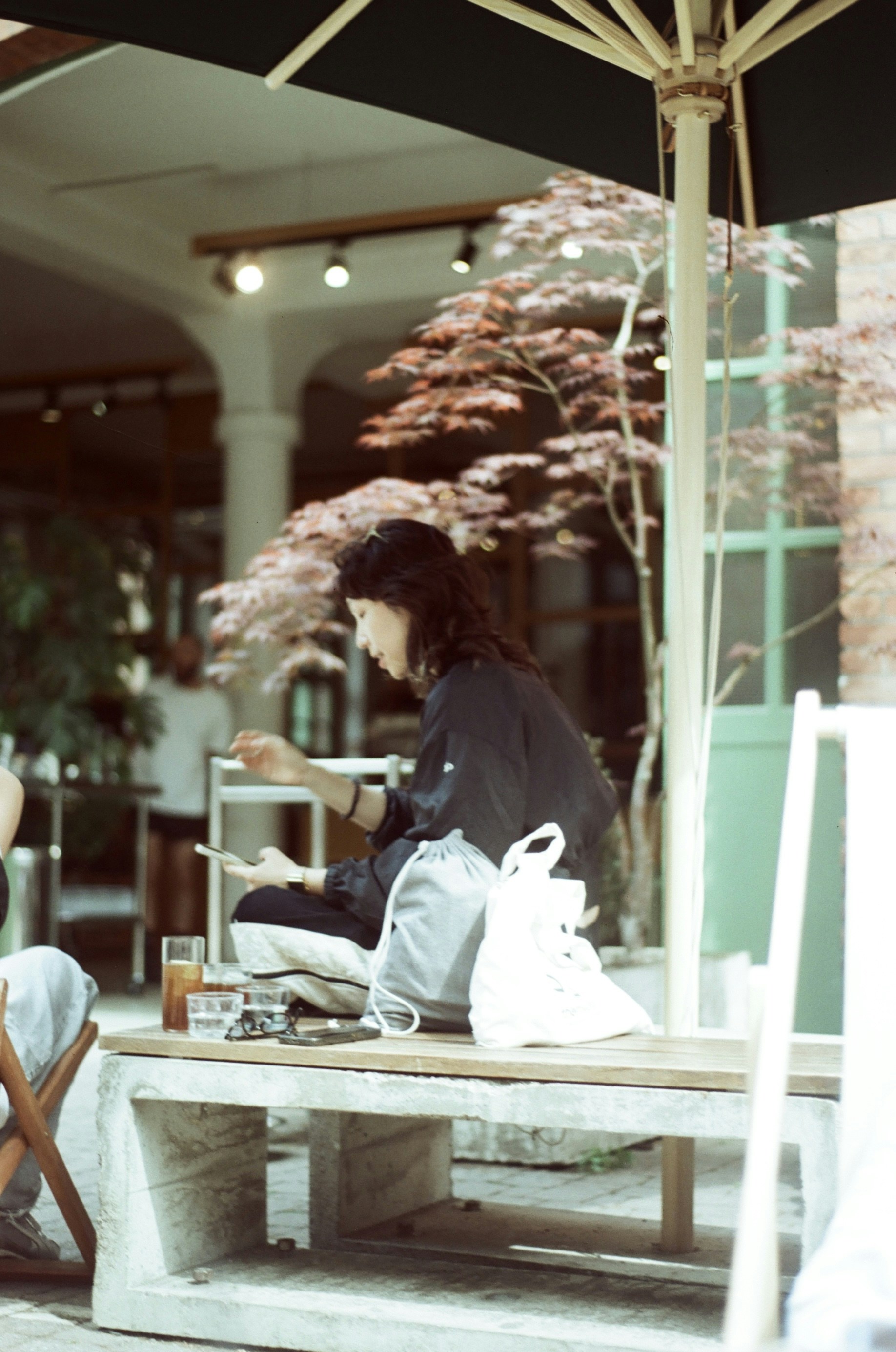 A person using a smartphone on a bench under a patio umbrella