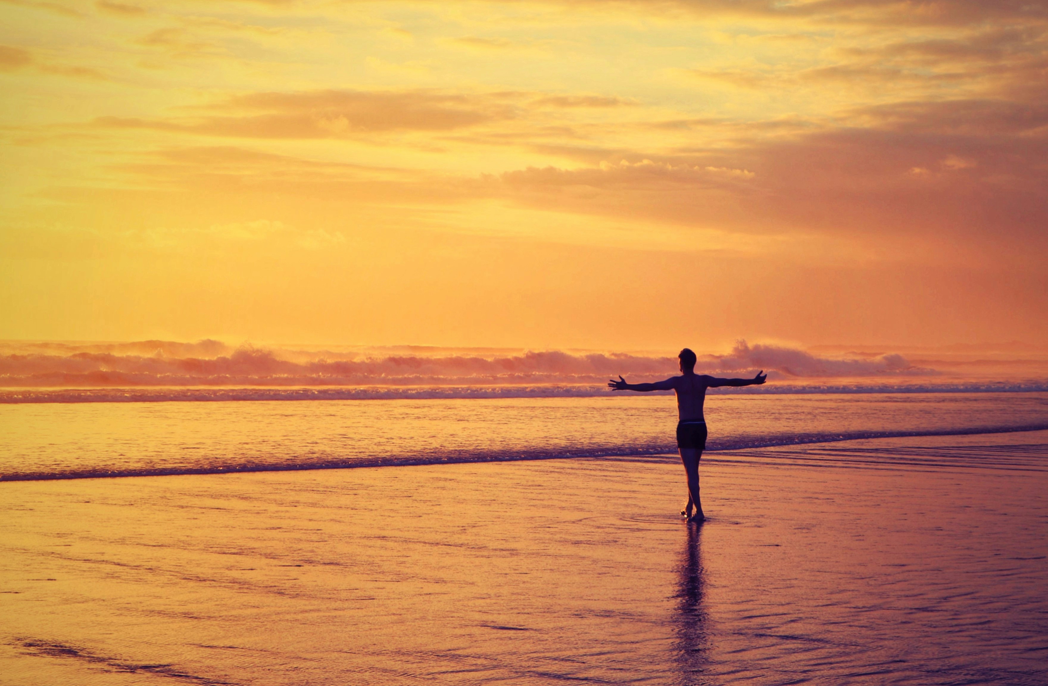 A person with arms outstretched walking on a beach at golden hour