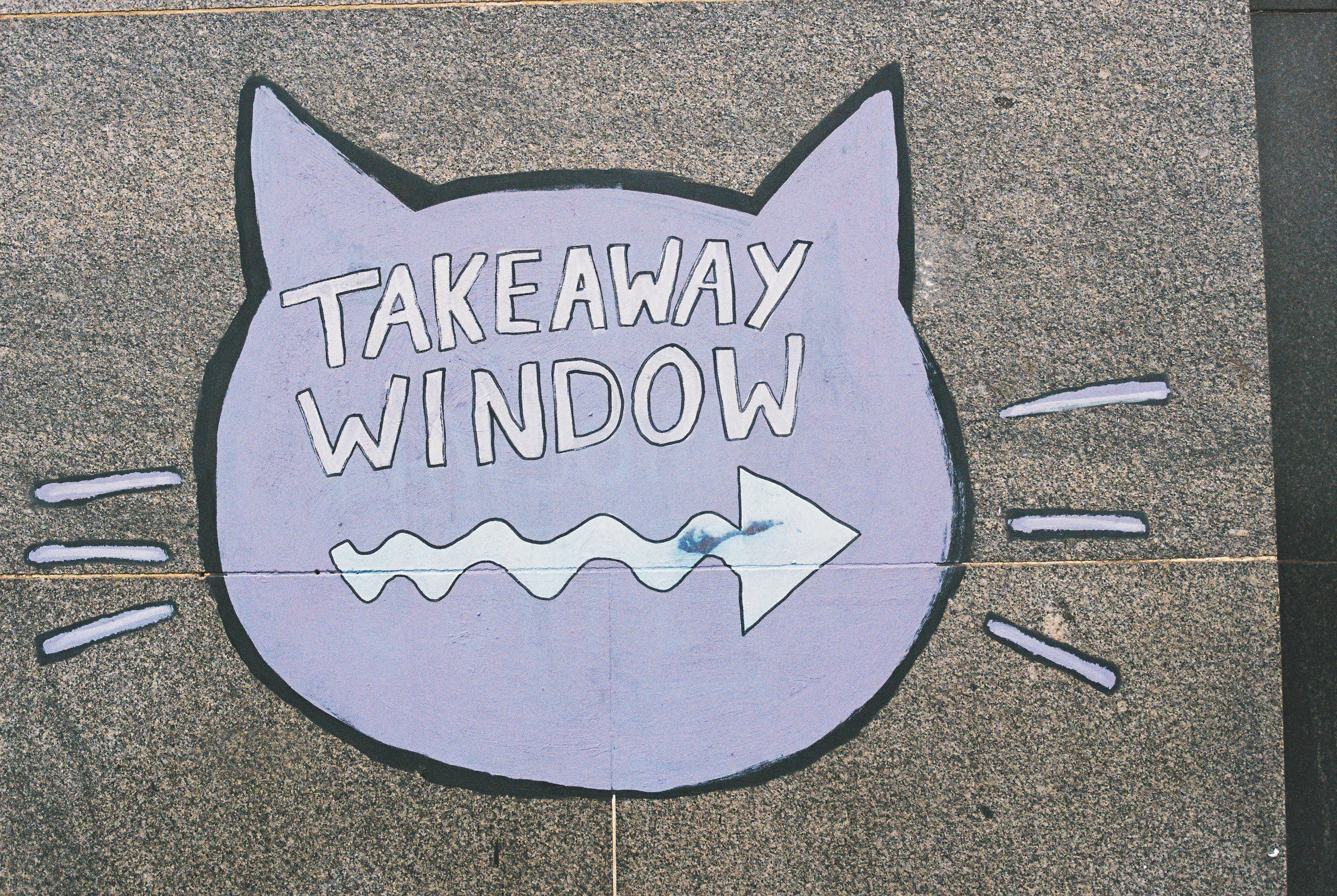 A purple cat-shaped sign reading "TAKEAWAY WINDOW" with a wavy arrow on stone