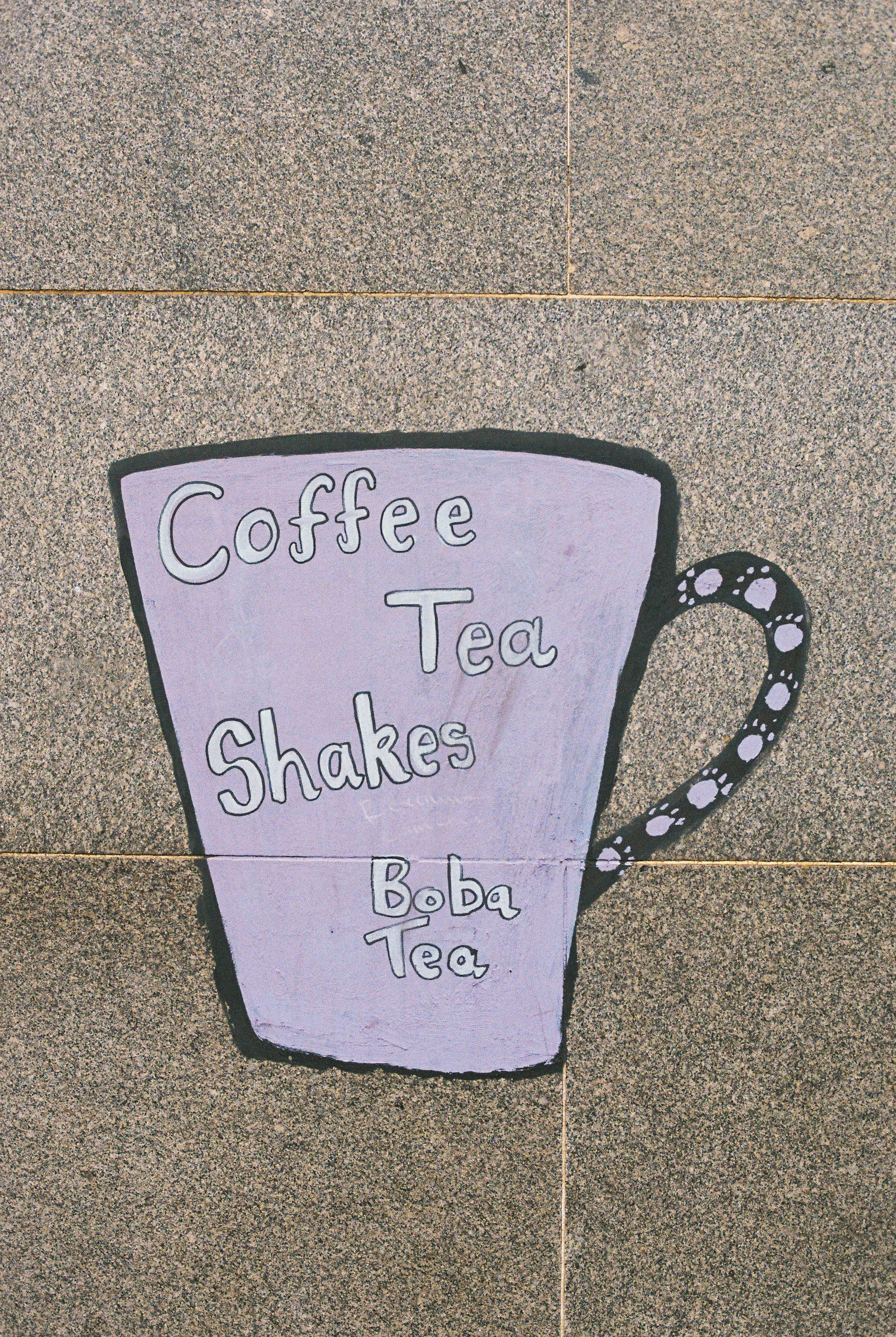 A purple cup painted on a stone wall reading "Coffee Tea Shakes Boba Tea"