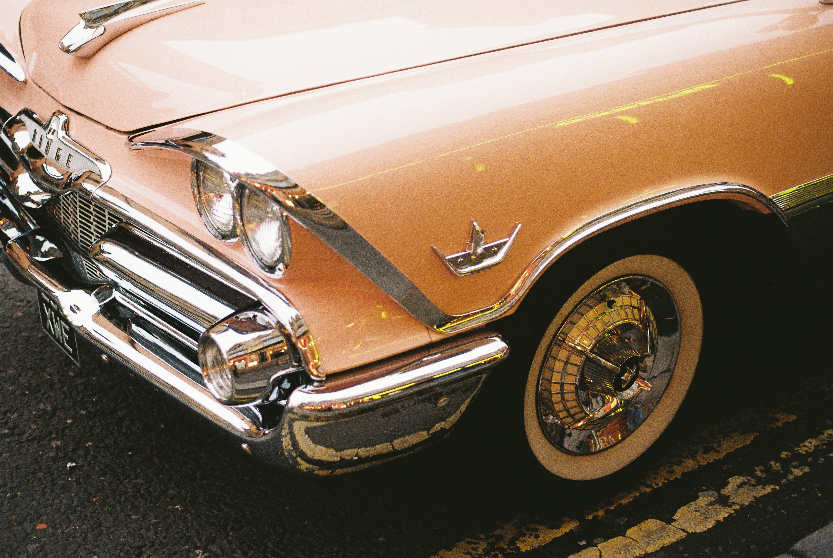 Photo of A pale pink vintage car with chrome trim and whitewall tires on asphalt by T
