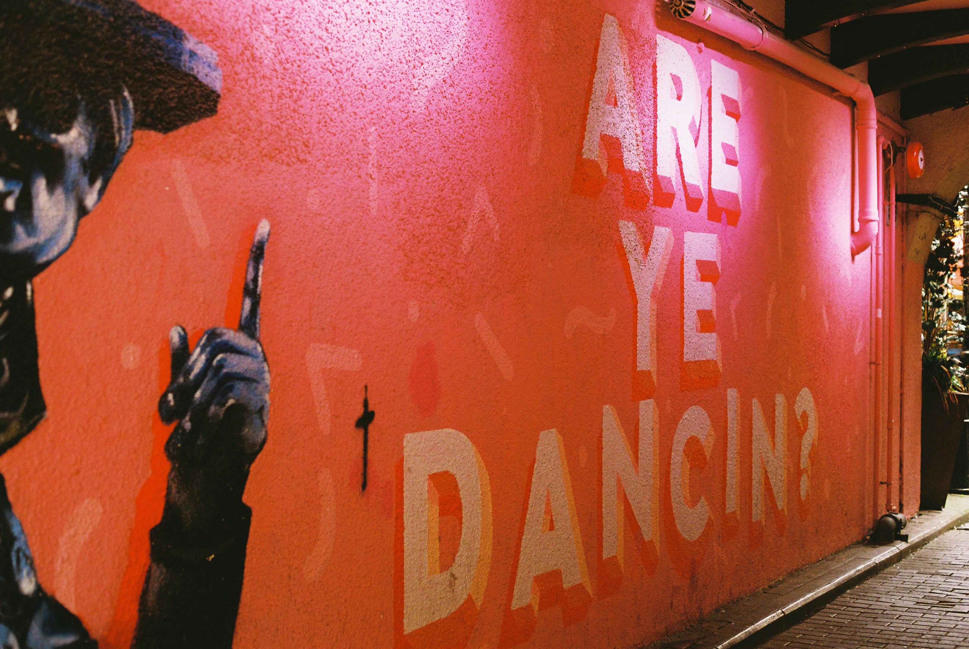 Une fresque murale rose avec des lettres blanches indiquant « ES-TU DANCÉE ? »