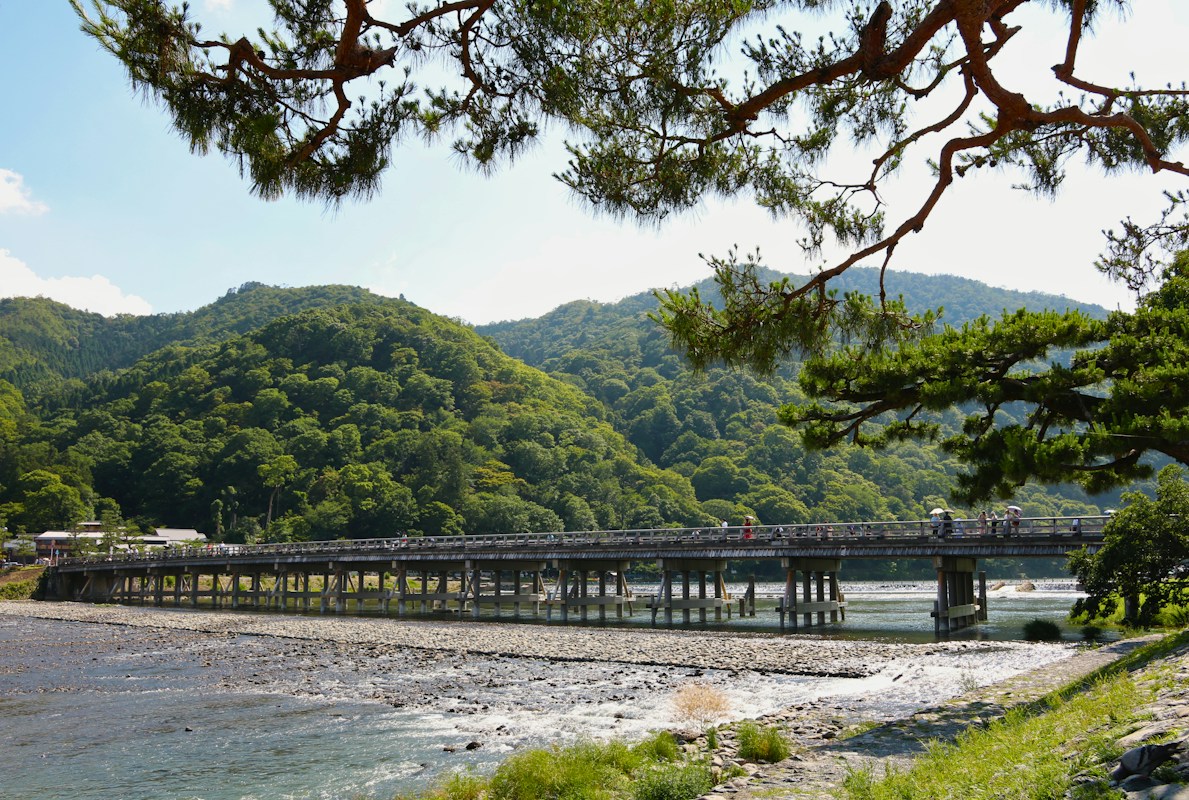 橫跨桂川的渡月橋，行人往來橋面，背景是嵐山山坡