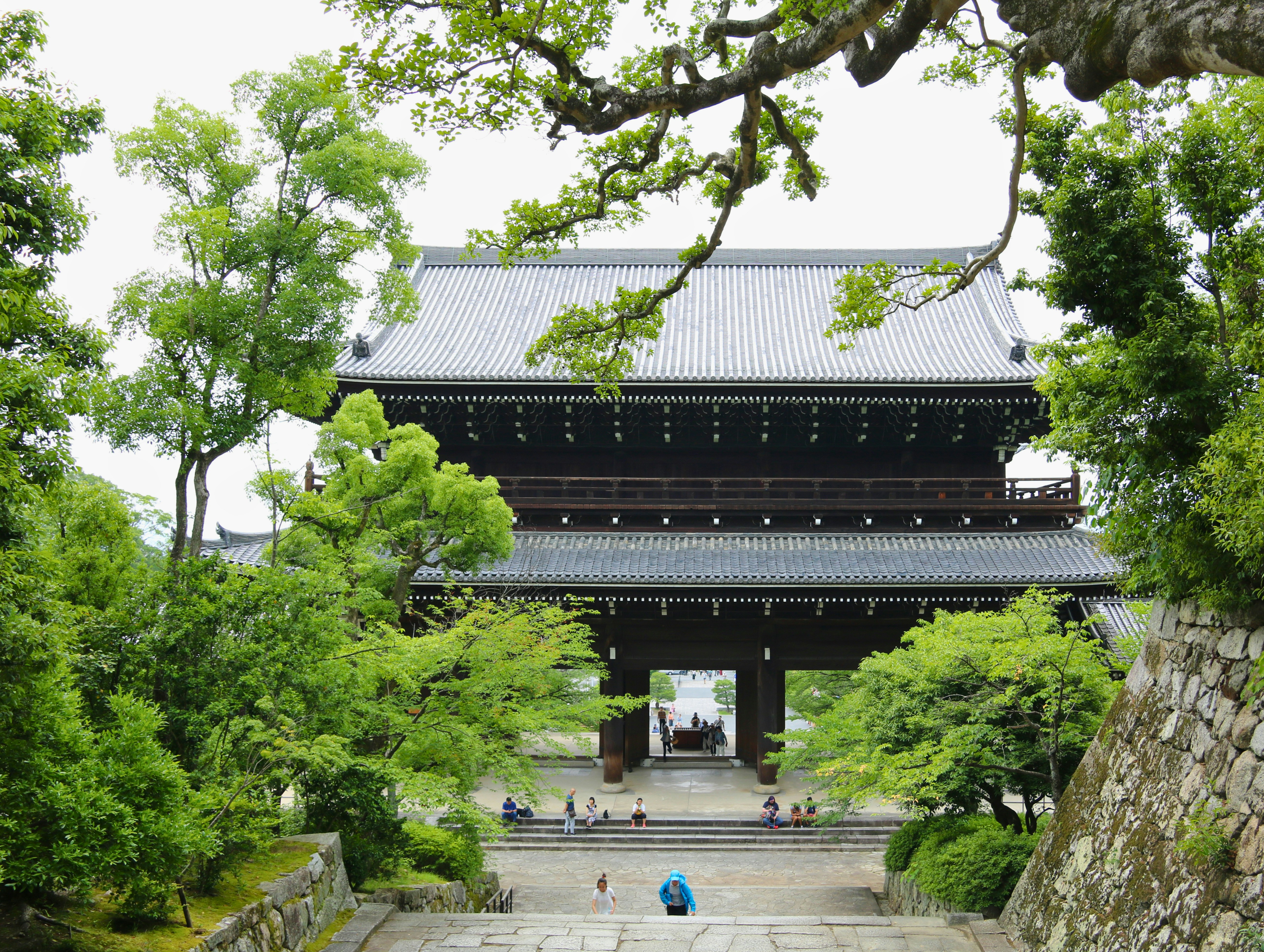 A large wooden temple gate with a tiled roof surrounded by lush green trees