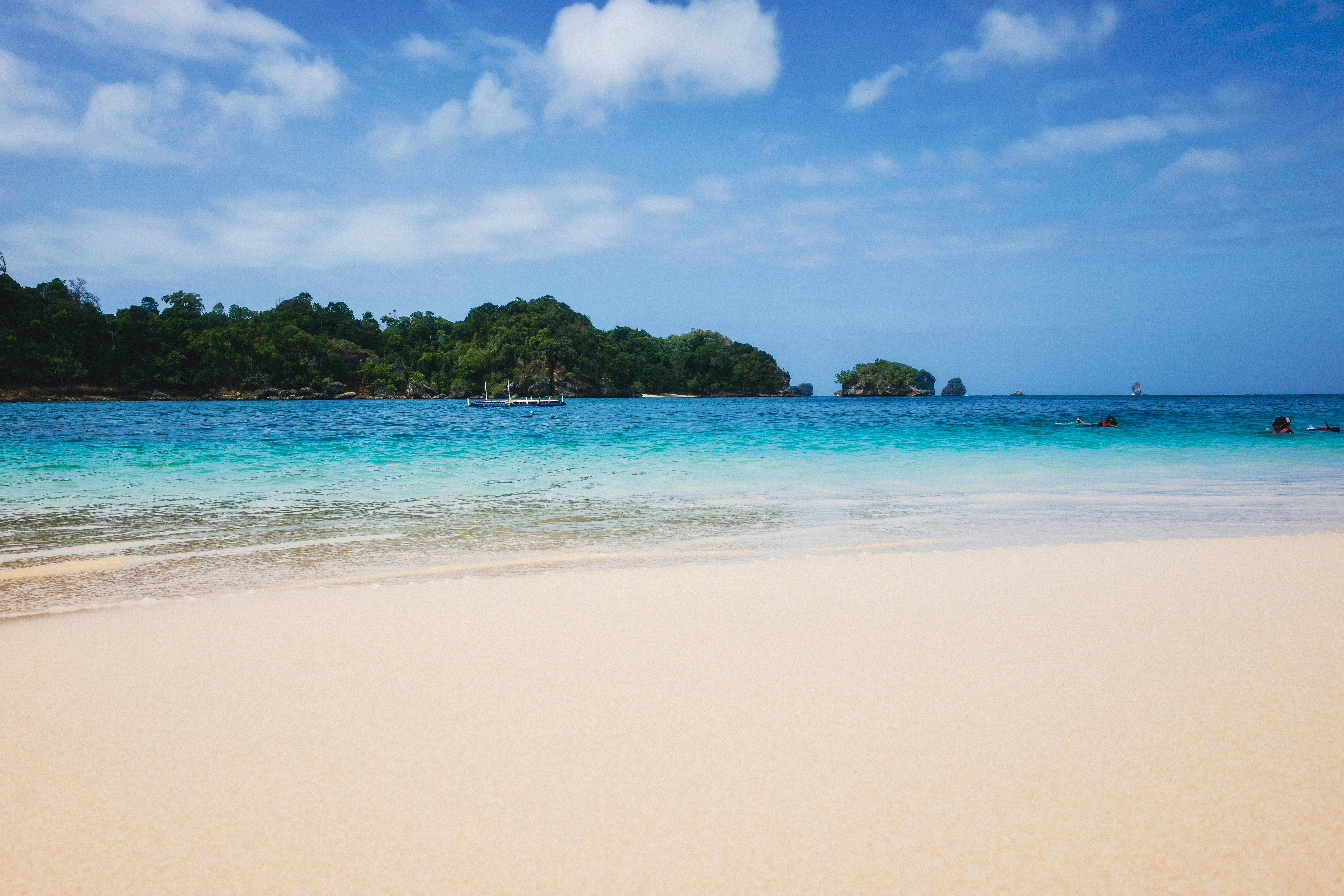 A sandy beach with turquoise water and forested islands under a blue sky