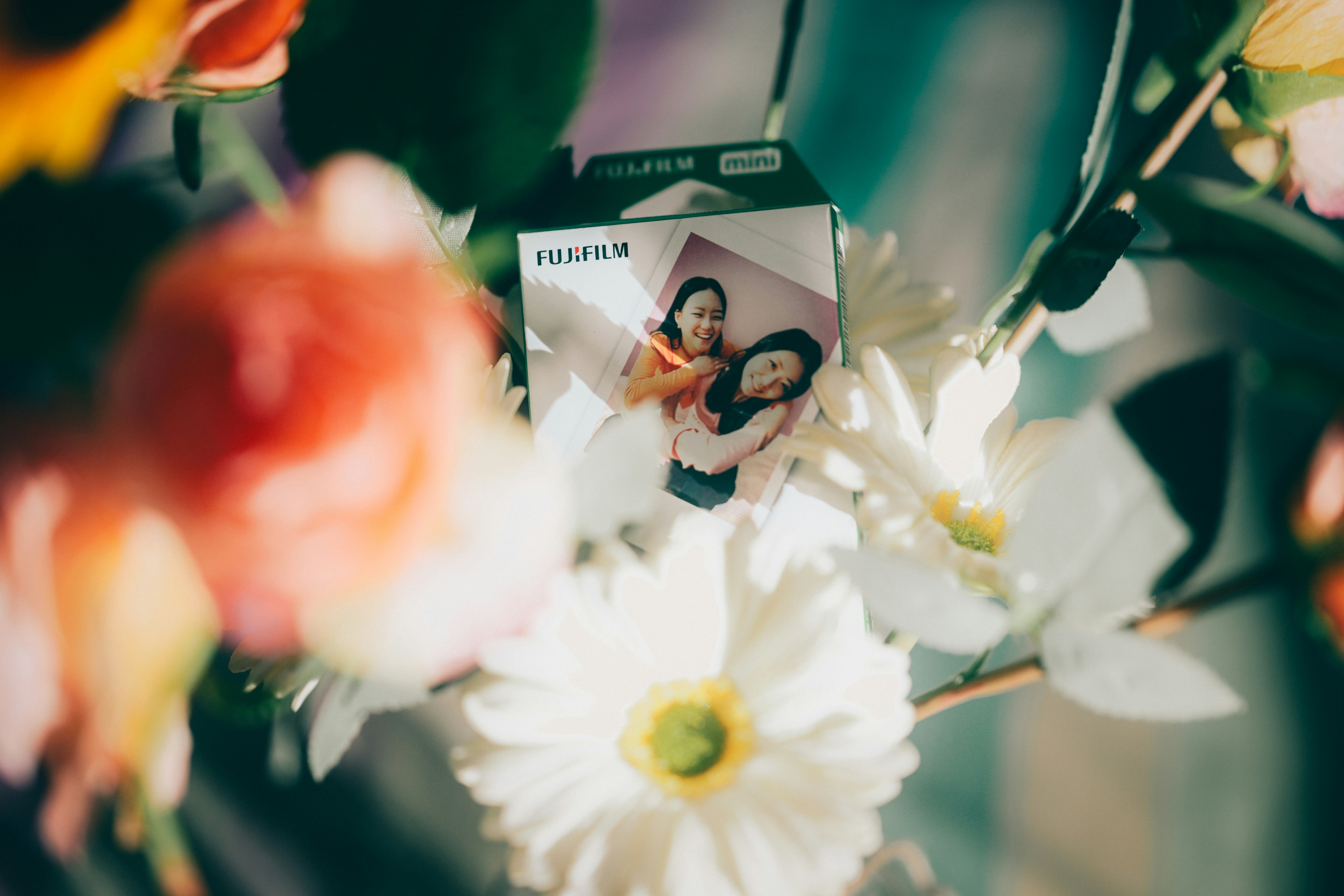 A Fujifilm Instax Mini film box nestled among white and orange flowers