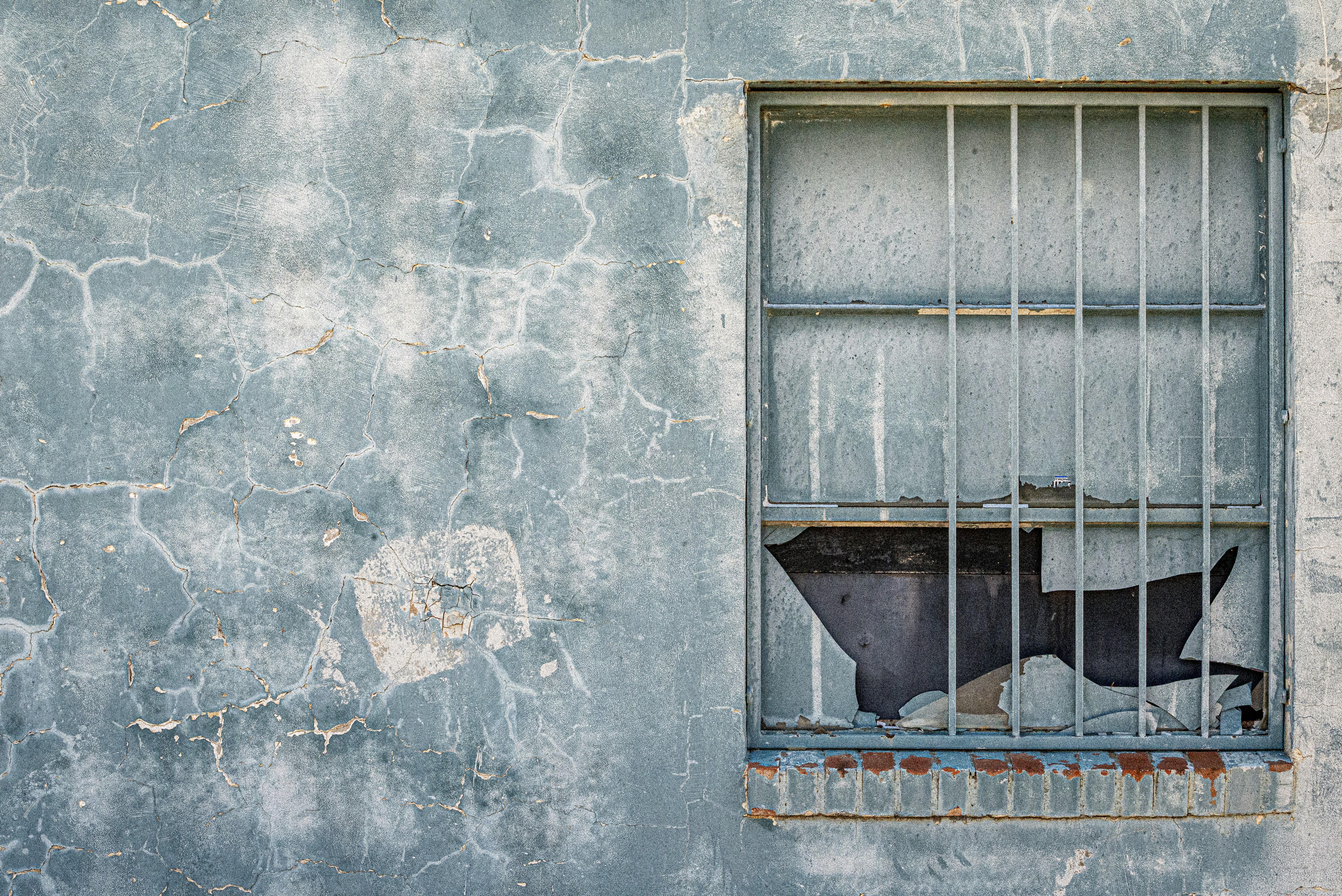 A weathered blue wall with cracked paint beside a window with metal bars