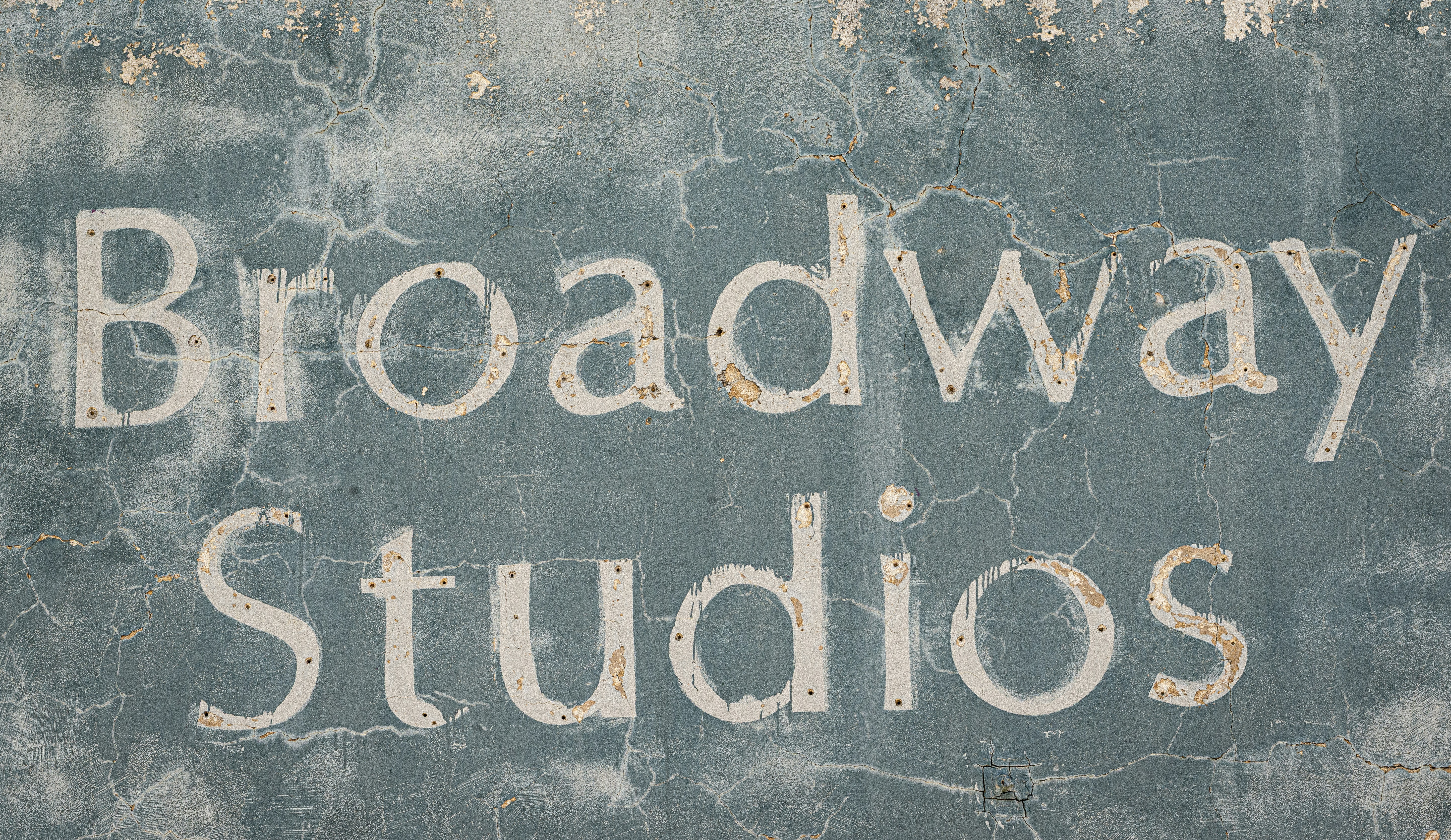 The words Broadway Studios painted in white on a weathered blue concrete wall