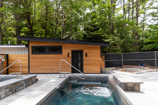 A small wooden cabin beside a stone-lined pool with a waterfall feature